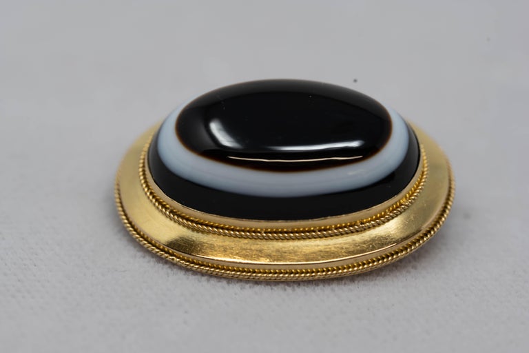 14k gold Victorian mourning brooch with Agate stone on the front and oval compartment on the back. Tested 14k, measures 32 mm long x 25 mm wide. Weighs 10.9 grams.
