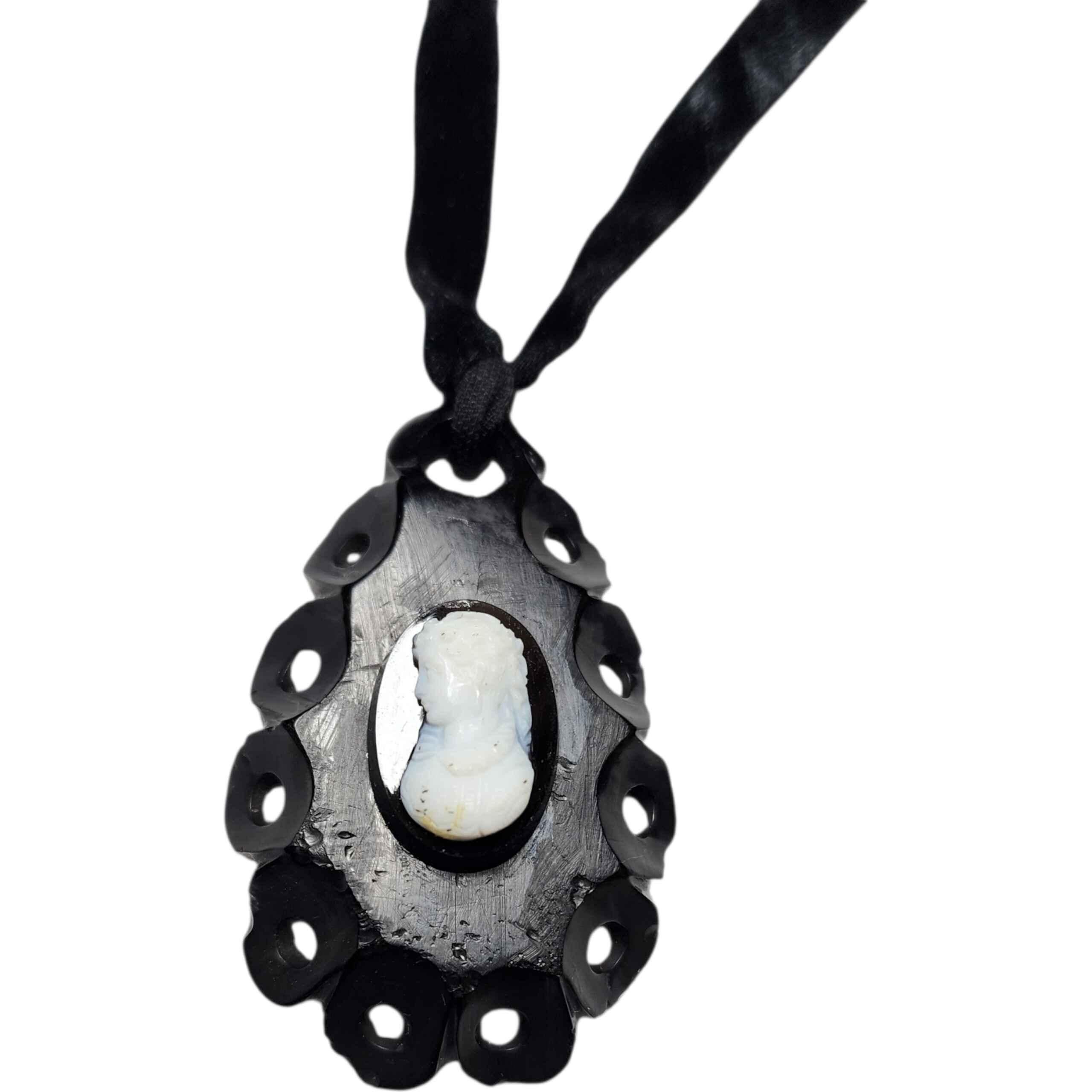 Ciondolo a lutto vittoriano su collana con nastro di velluto - cammeo a conchiglia intagliato a mano, montatura nera Whitby Jet, 1880 ca.

Questo ciondolo, un esempio di gioielleria vittoriana per il lutto, presenta un cammeo di conchiglia bianca