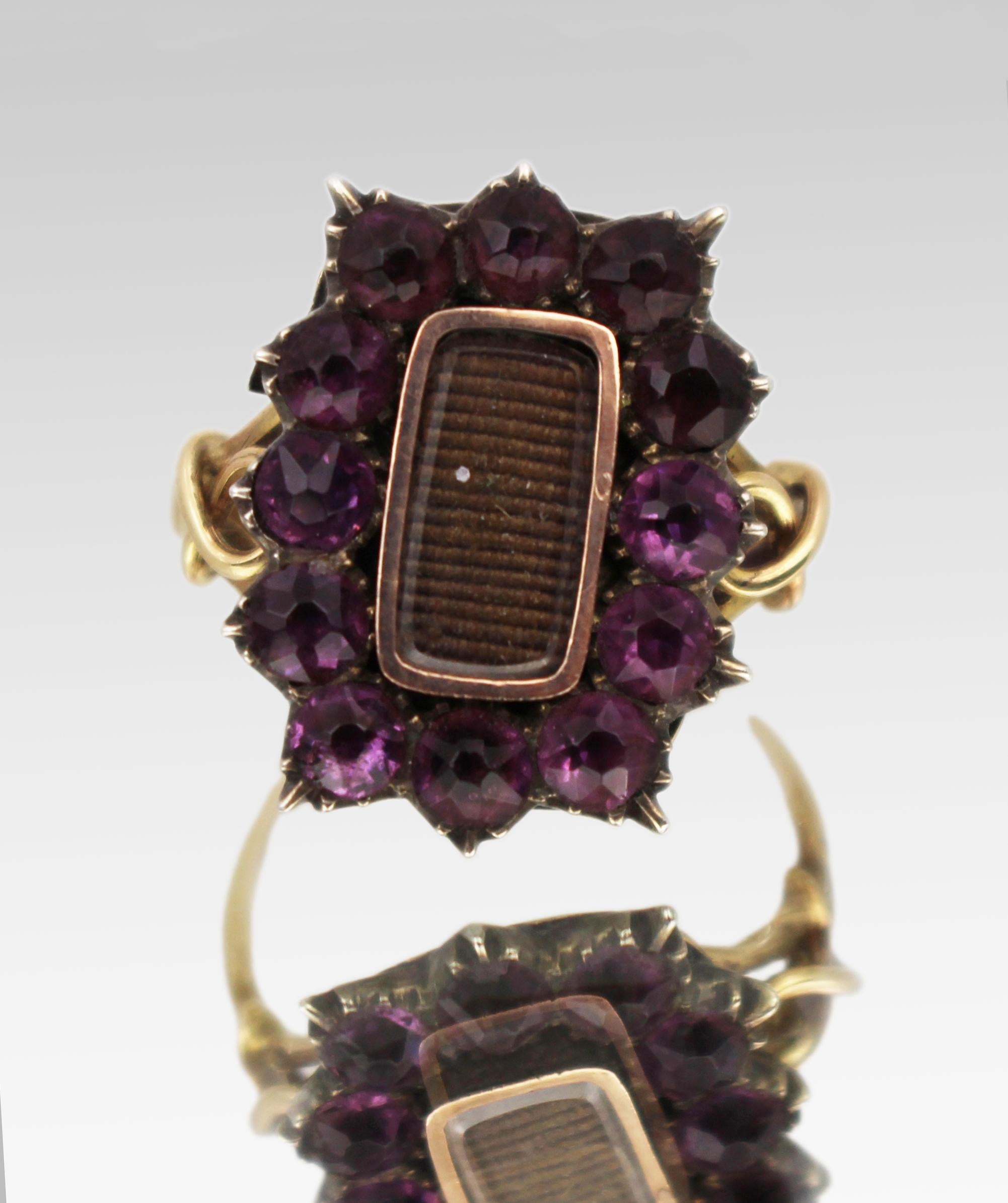Victorian Mourning Ring with Purple Glass Stones

A striking example of Victorian mourning jewellery, this ring features a central cluster of twelve purple glass (paste) stones, each set in pinch-style settings arranged in a cushion-shaped design.