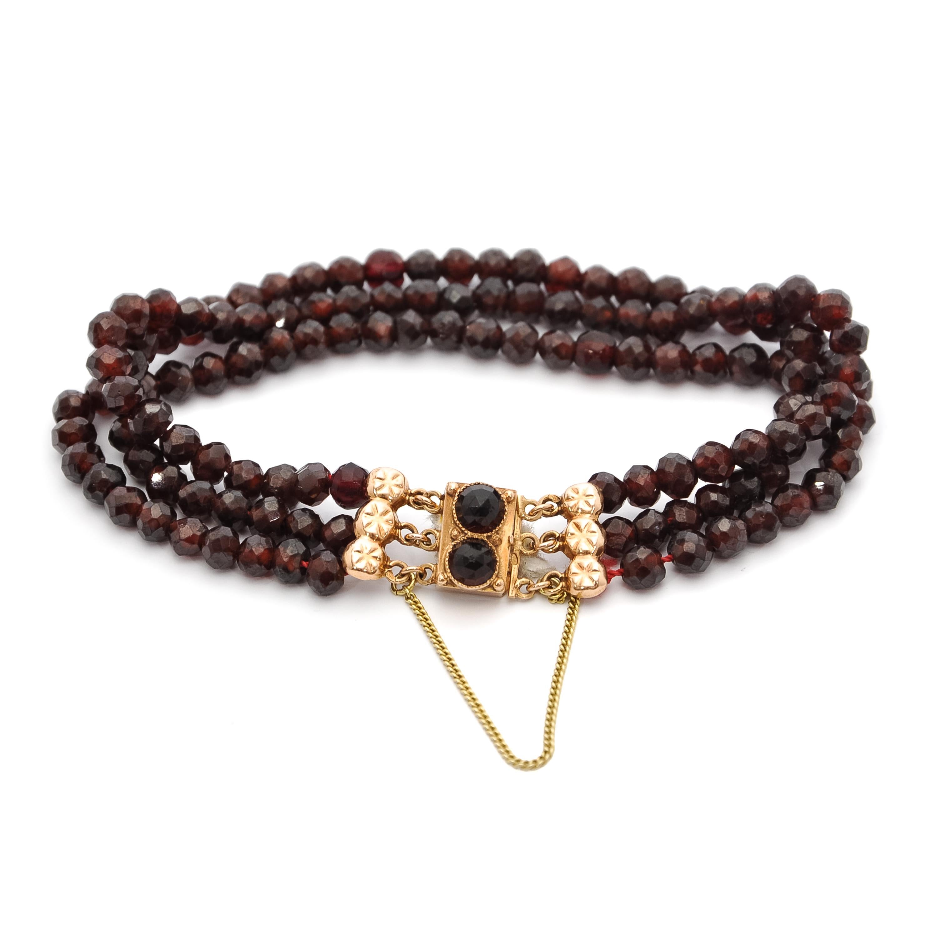 A three-strand 14 karat yellow gold garnet bracelet. The clasp of this bracelet is beautifully detailed. The raised center of the clasp is surrounded with a twisted gold ribbon. At the end of each string a small gold detail is attached between the