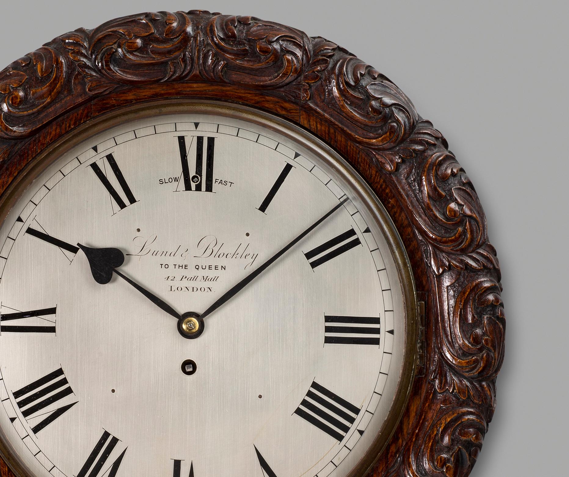 A fine quality antique, Victorian oak cased wall timepiece by this well-known clockmaking partnership. The substantial circular solid oak case has a surround to the dial, exceptionally well carved with flowing scrollwork and foliage. The 12 inch