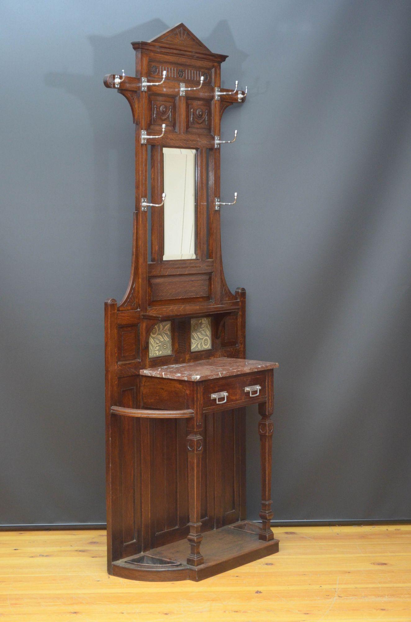 St041 Stylish Victorian coat stand in oak in the manner of Christopher Dresser, having architectural pediment with sunray carvings above panelled and fielded back with beehive style hooks, above two original tiles, marble top and a drawer, all