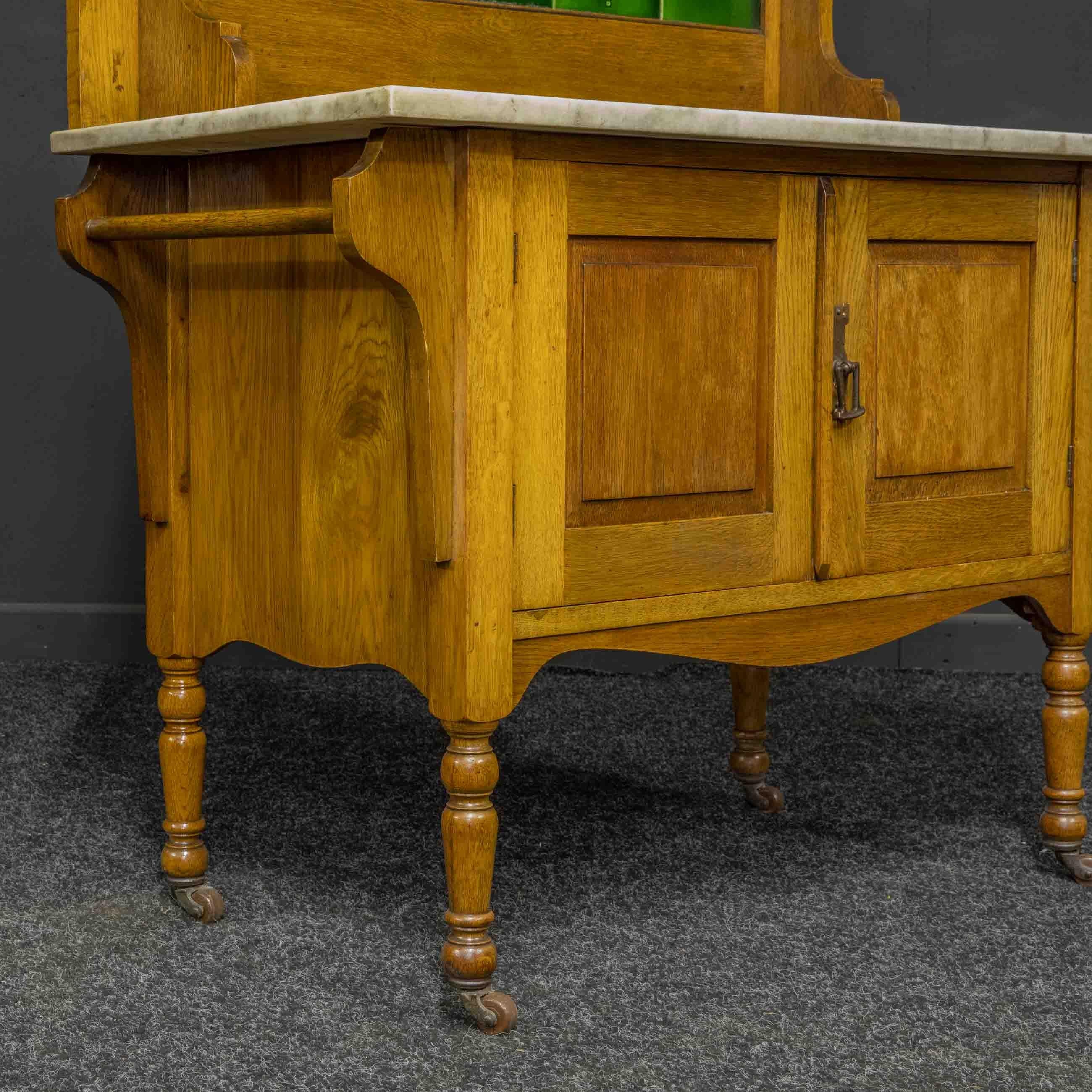 A golden oak washstand from the late Victorian period. Complete with the original towel rails to the sides of a two cupboard door base, sat on turned legs with it's castors retained. The figured white marble top is in good order and is set off with