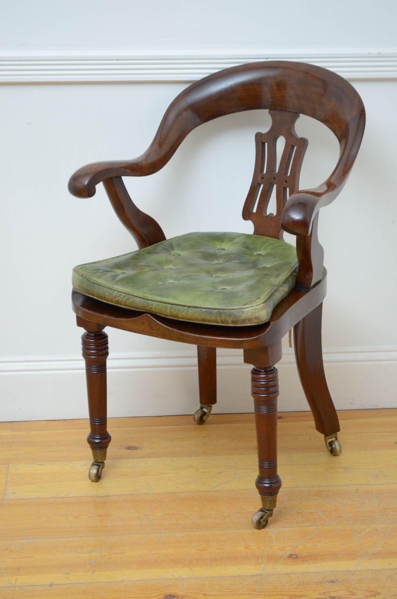 Sn5283 Victorian office chair or desk chair, having shaped back rail with carved centre splat and downswept arms and generous seat with green leather cushion, all standing on turned and ringed legs and castors. This antique chair retains its