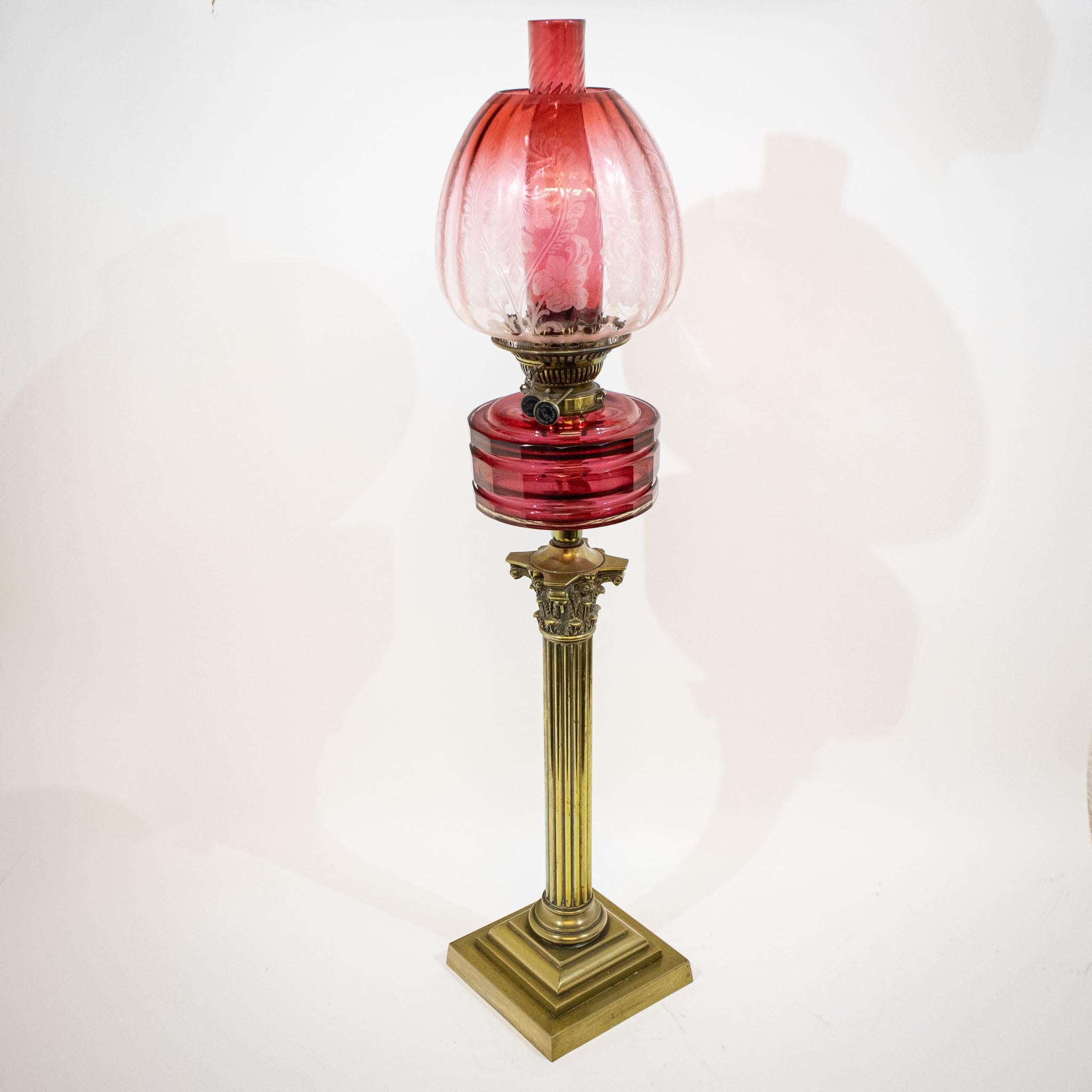 A fabulous quality 19th century oil lamp with original cranberry glass shade and burner on a heavy brass Corinthian column base.

- Heavy faceted cranberry glass oil reservoir.
- Twin oil adjusters are marked 