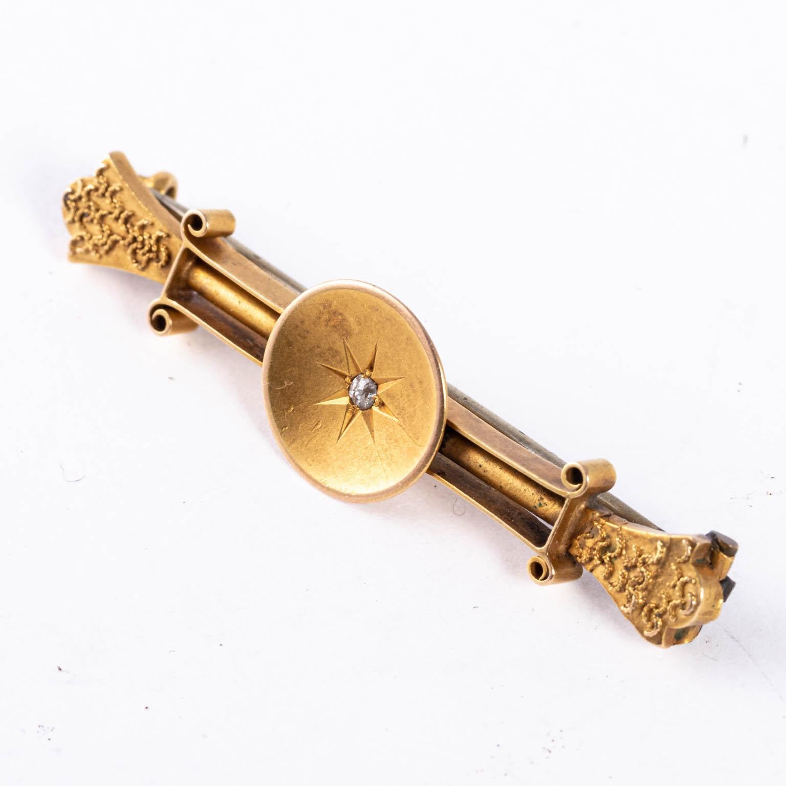 Circa 1890s Victorian bar pin that features a small European cut diamond in the center flanked by decorative scrollwork.