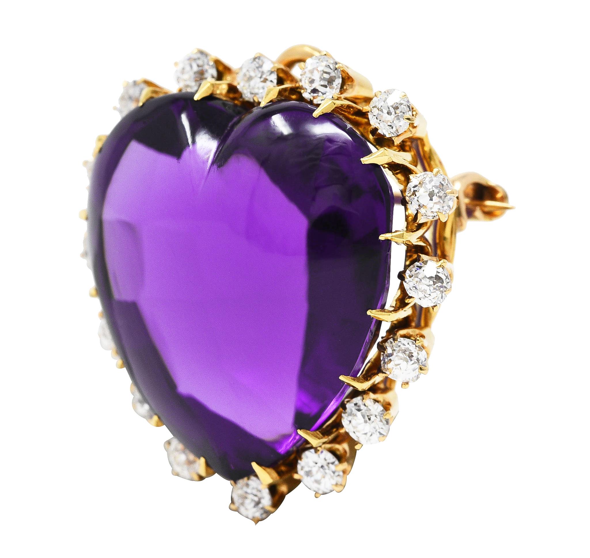 Centering a 20.0 mm heart shaped amethyst cabochon - transparent dark purple in color. Set with talon prongs and featuring a halo surround of old mine cut diamonds. Weighing approximately 0.96 carat total - H/I color with VS2 clarity. Prong set