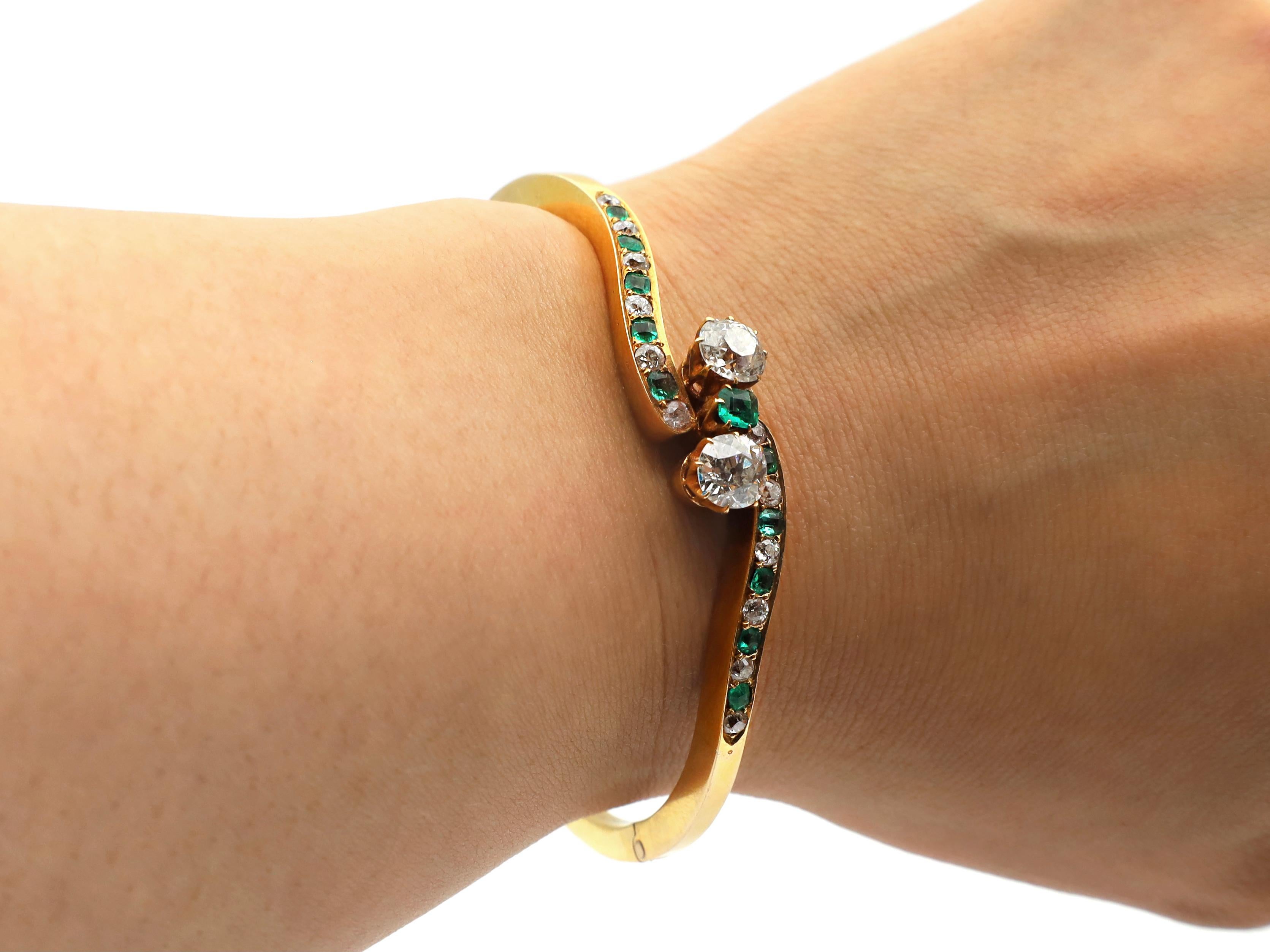 Victorian Old Mine cut diamond and emerald two stone twist hinged bangle in 18kt yellow gold. A hinged bangle with a square profile fitted to the front with two cushion shape Old Mine cut diamonds in claw settings, centred with a round mixed cut