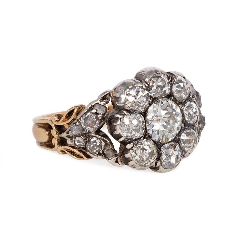 An antique old mine cut diamond cluster ring designed as a flowerhead with diamond-set foliate shoulders, in silver-topped 15K gold.  England.  Atw 1.50 ct.

Top measures approximately 13mm across
Current ring size: US 6 3/4 (Please contact us with