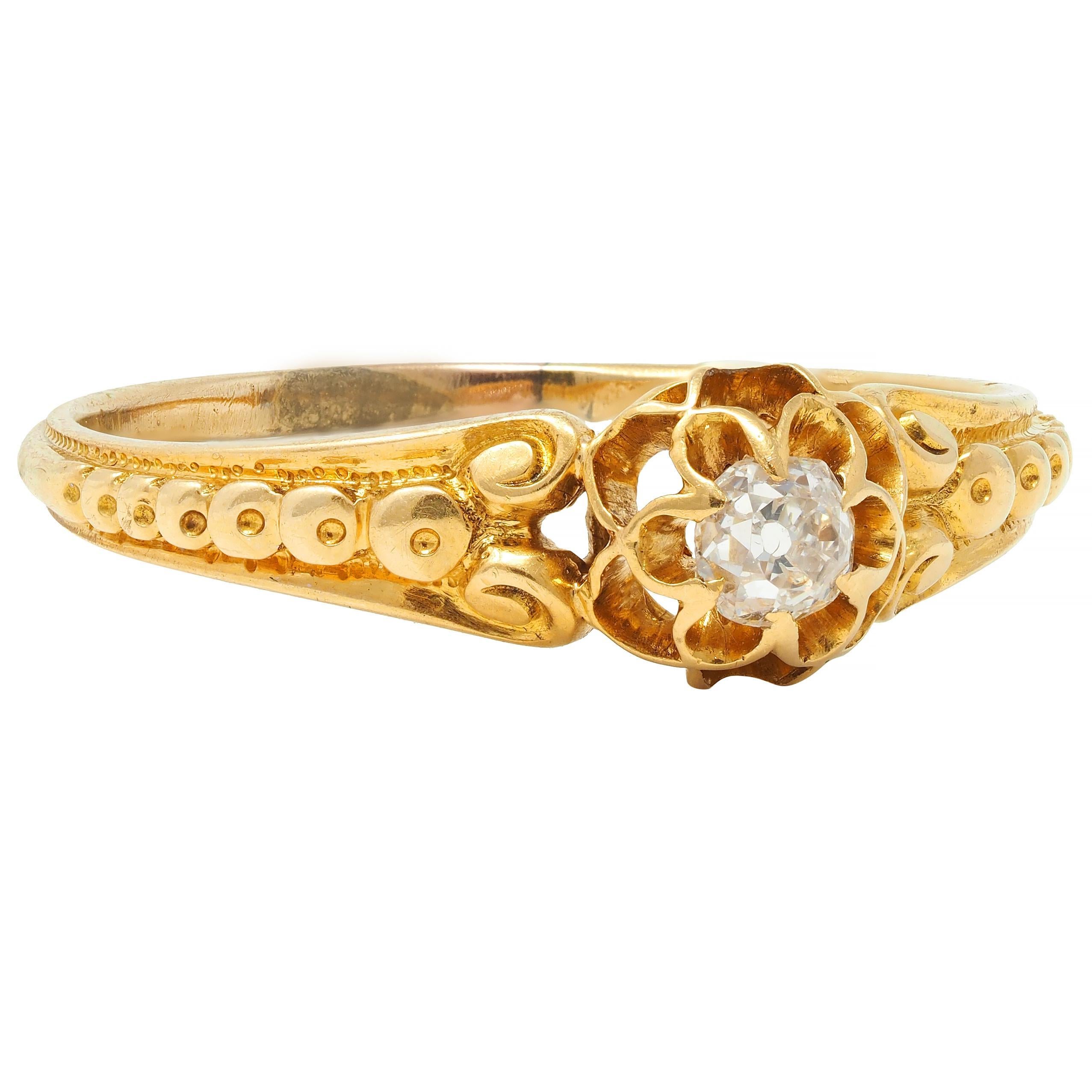 Centering and old mine cut diamond weighing approximately 0.15 carat total 
G color with VS2 clarity - set with buttercup motif belcher prongs 
With pierced gallery and flanked by scrolling volute shoulders
Accented by gold bead detailing 
Complete