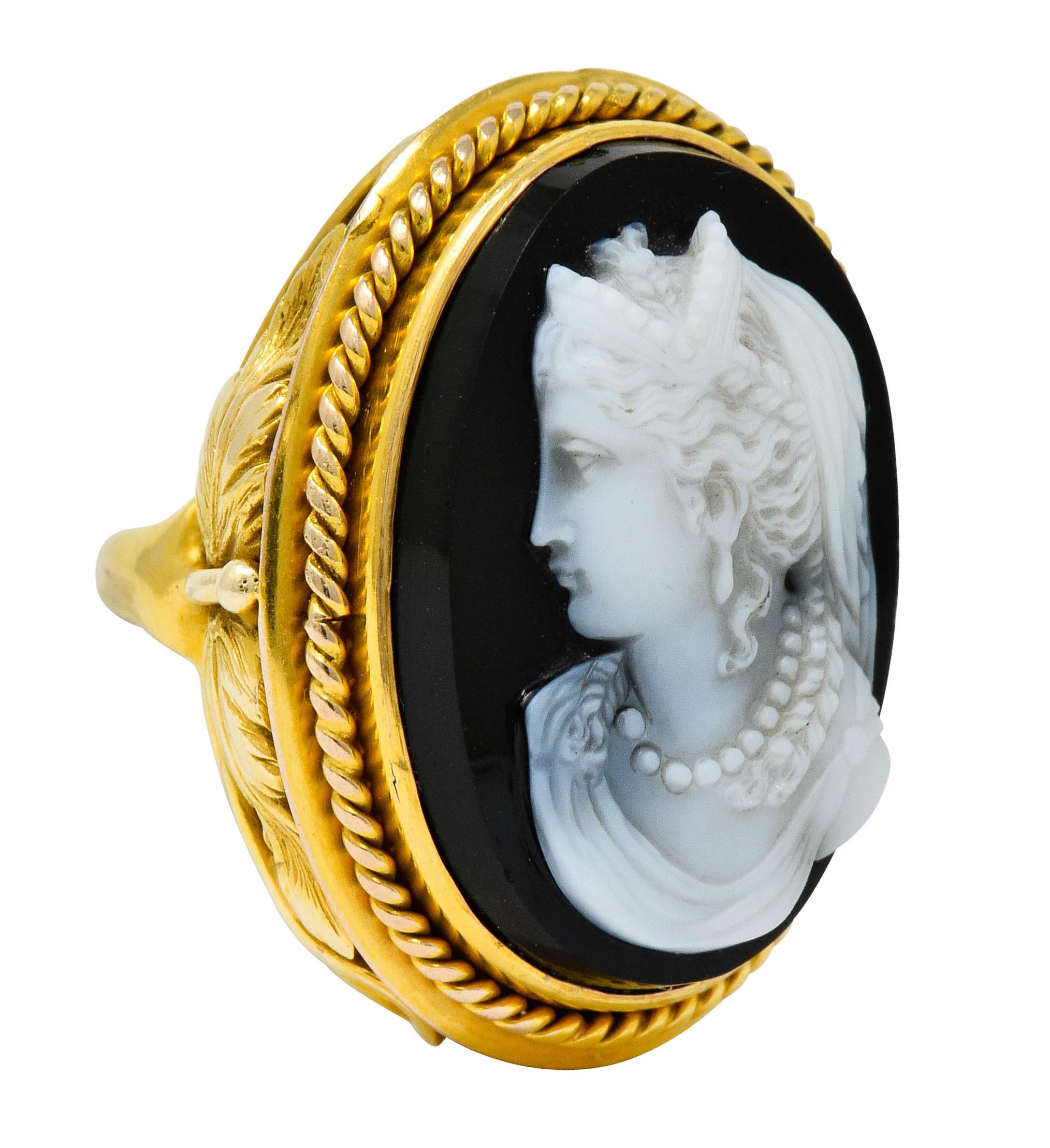 Centering an oval tablet of banded onyx agate measuring approximately 23.2 x 16.7 mm

Depicting an elegantly dressed woman deeply carved in matte white with a glossy black background

Bezel set in a polished gold surround with a twisted rope motif
