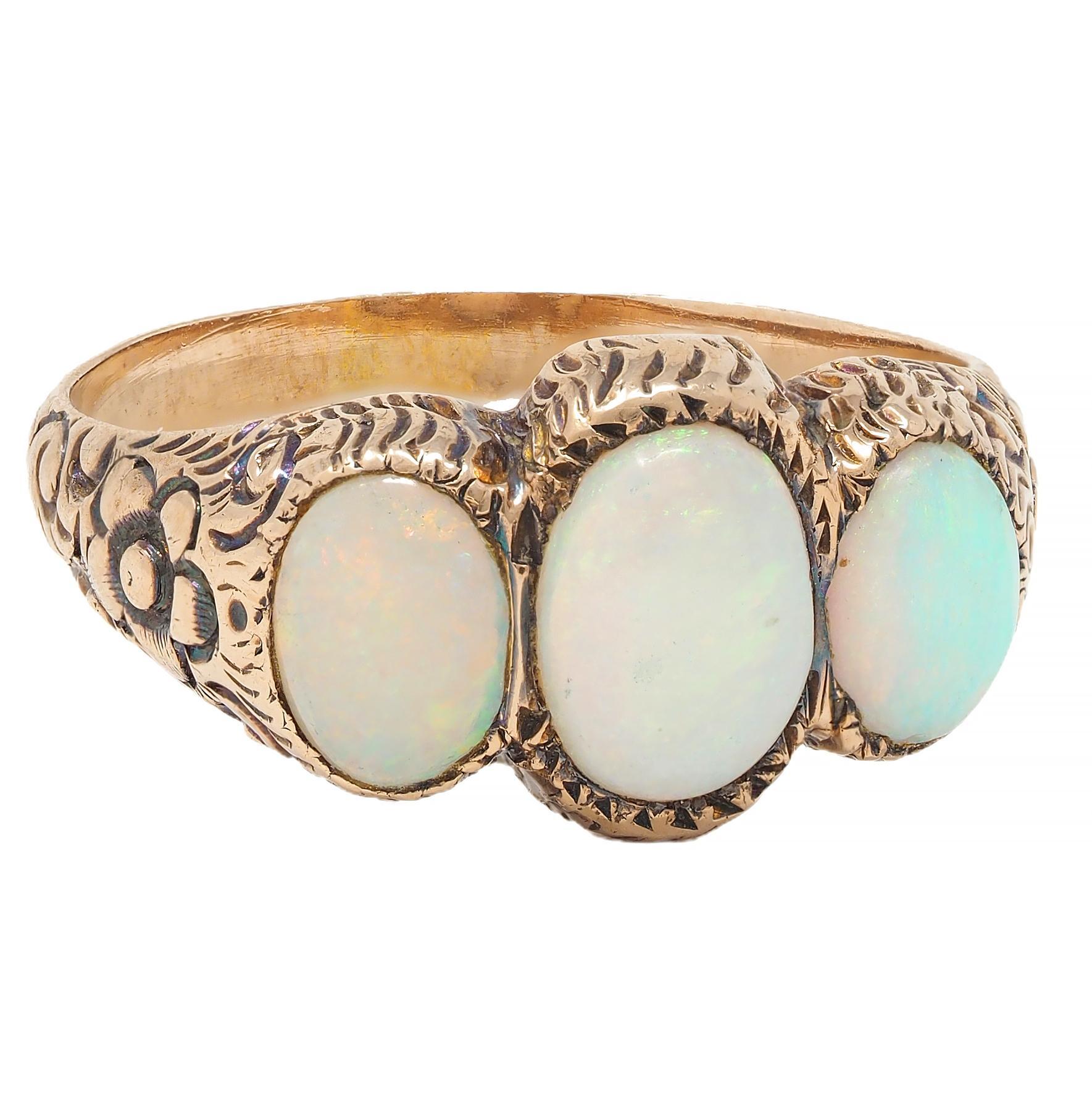 Centering three oval-shaped opal cabochons flush set east to west
Graduating in size from 4.0 x 6.0 mm to 5.0 x 7.0 mm 
White body color with spectral play-of-color 
With engraved gallery and shoulders
Displaying floral and scroll motifs
Tested as