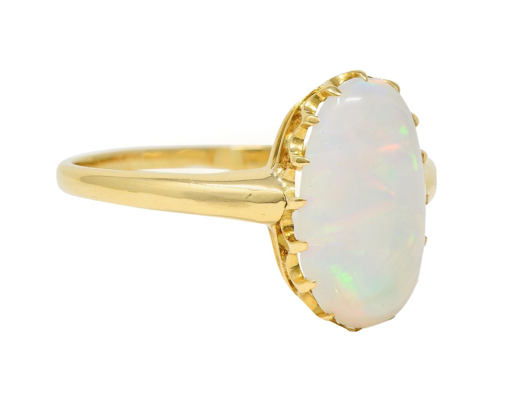 Centering an oval-shaped opal cabochon measuring 3.2 x 7.8 mm 
Translucent white in body color with strong spectral play-of-color
Set with talon prongs in a pierced gallery 
Flanked by rounded shoulders
With high polish finish
Tested as 18 karat