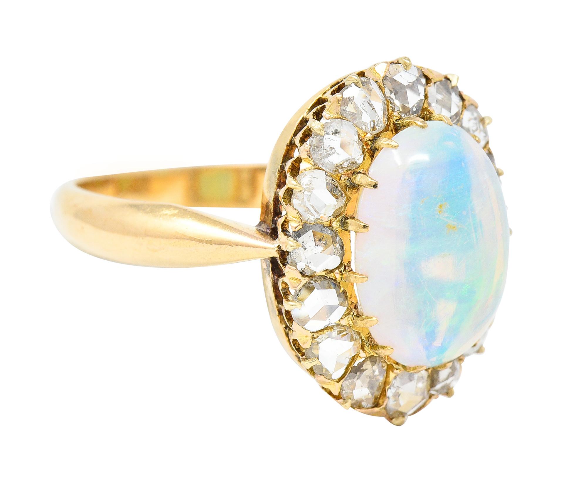 Centering an oval shaped opal cabochon measuring 8.25 x 11.75 mm. Translucent white in body color with spectral play-of-color. Prong set with a halo surround of rose cut diamonds. Weighing approximately 1.30 carats total. H/I color with VS2 clarity.
