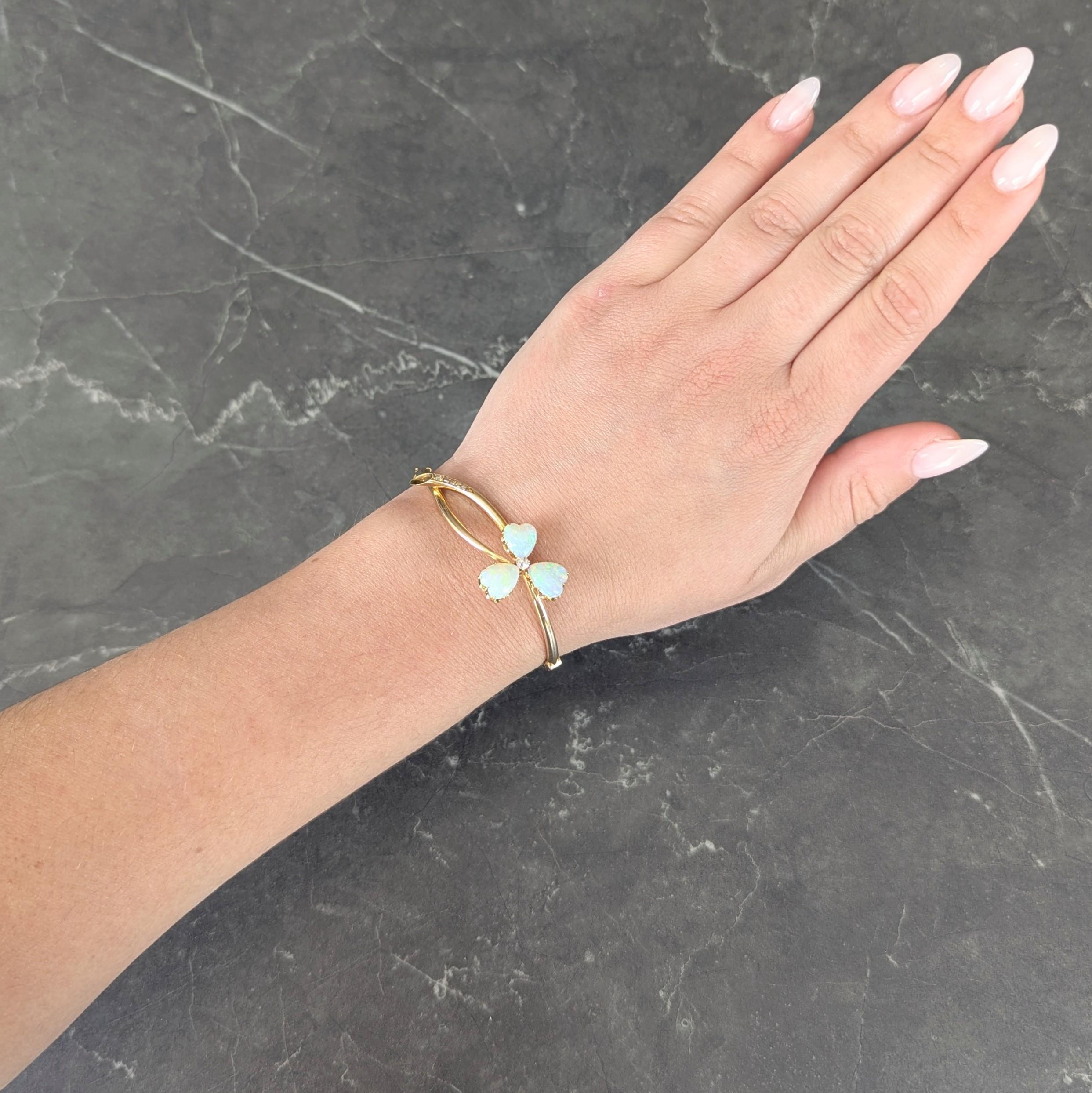 Designed as a bypass-style bangle terminating with clover and stem
Featuring three heart shaped opals measuring 8.0 x 10.0 mm - prong set
Translucent white in body color with spectral play-of-color
Centering an old mine cut diamond weighing