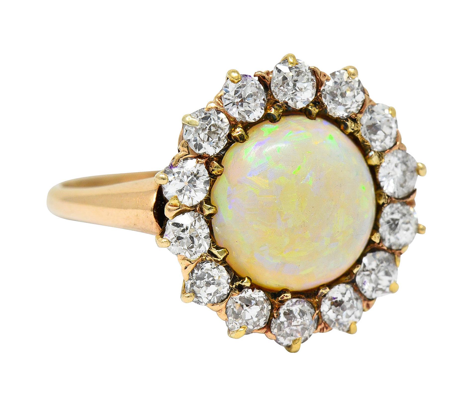 Cluster ring centers a round cabochon of opal measuring approximately 7.5 mm

Translucent and white in body color with very strong spectral play-of-color

Surrounded by a halo of old European and mine cut diamonds

Weighing in total approximately