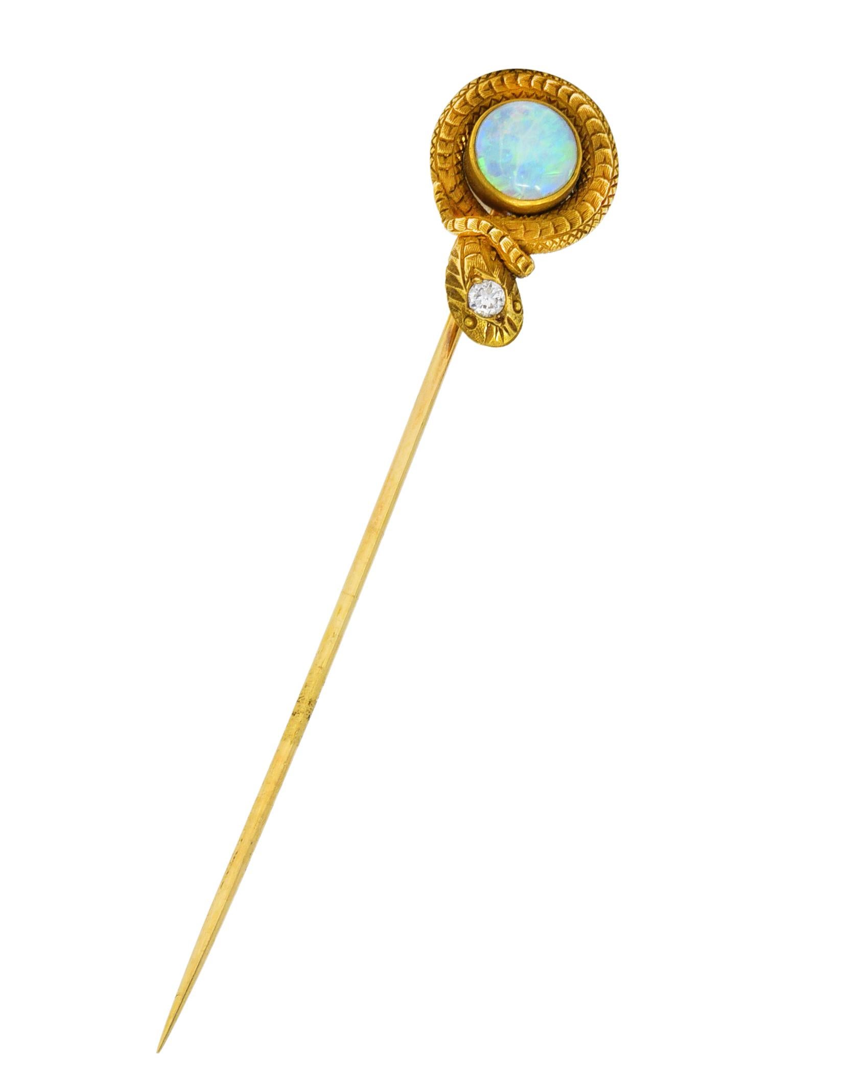 Stickpin is designed as a stylized snake with texturous scales and expressive features. Coiled around a bezel set 6.5 mm round opal cabochon. Translucent white in body color with excellent spectral play-of-color. Accented by an old European cut