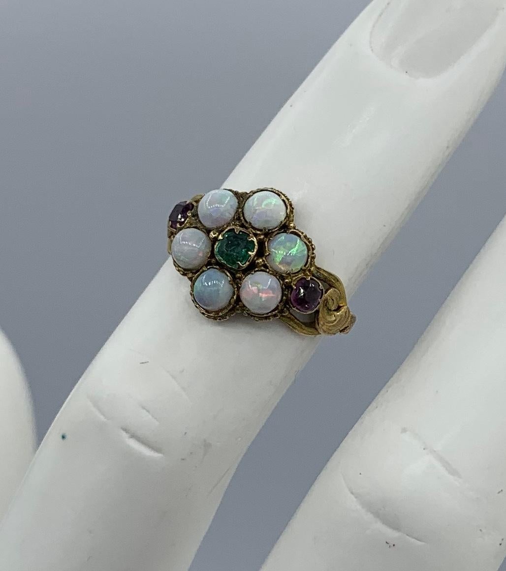 This is a beautiful Antique Victorian Ring with a central Emerald surrounded by a halo of six gorgeous natural round Opals of incredible color and stunning beauty.   The effect is of a jeweled flower.  On either side of the opals are fine natural