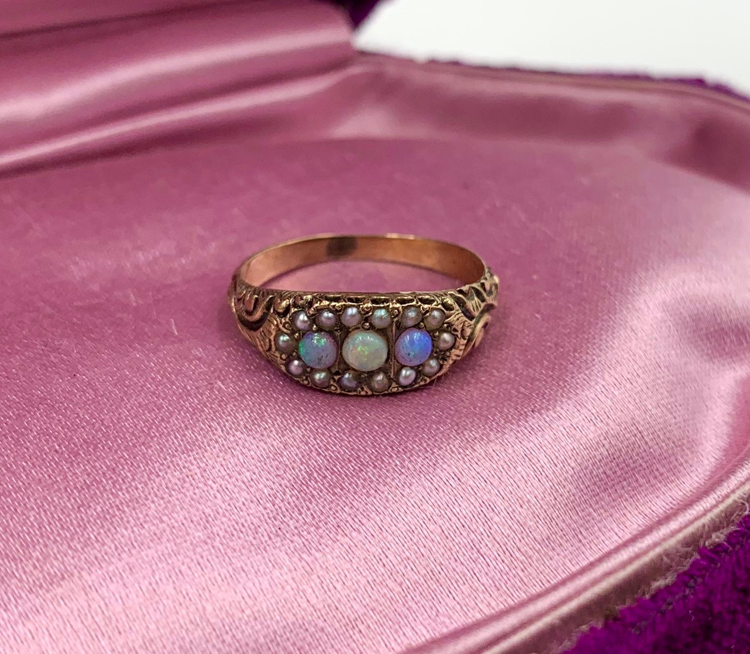An Antique Victorian - Edwardian Ring with three gorgeous natural round Opals of stunning beauty. The three Opal gems are accented by a halo of Seed Pearls.   The jewels are set in a gorgeous engraved scroll motif setting in 10 Karat Rose Gold. 