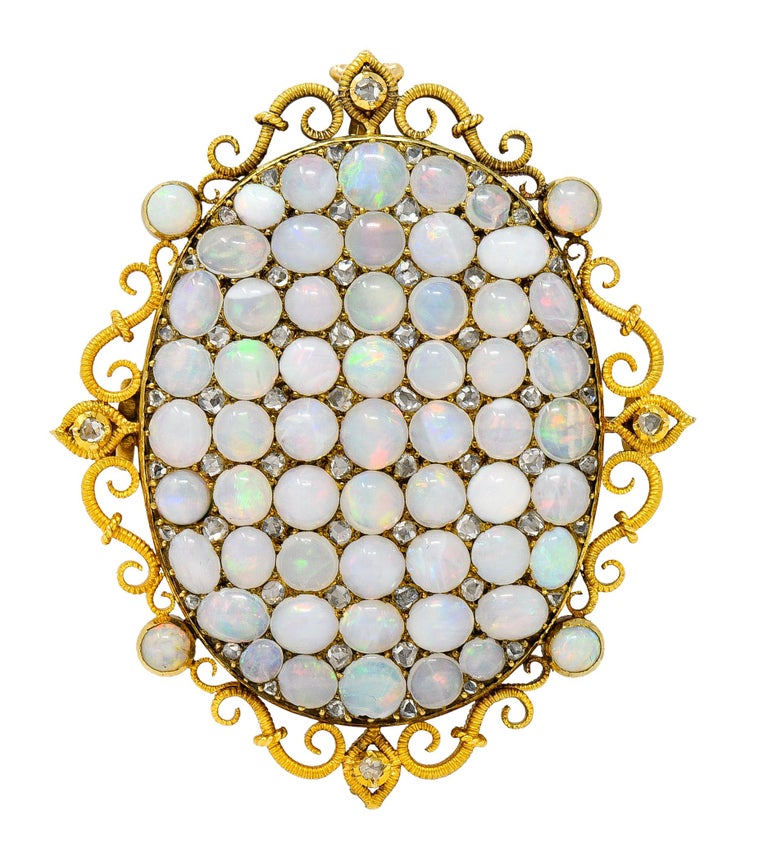 Ornate brooch is designed as an oval pavè field comprised of opal cabochons with rose cut diamonds. With a scrolling gold surround accented by additional opals and diamonds - deeply ridged in texture. Total diamond weight is approximately 0.50 carat