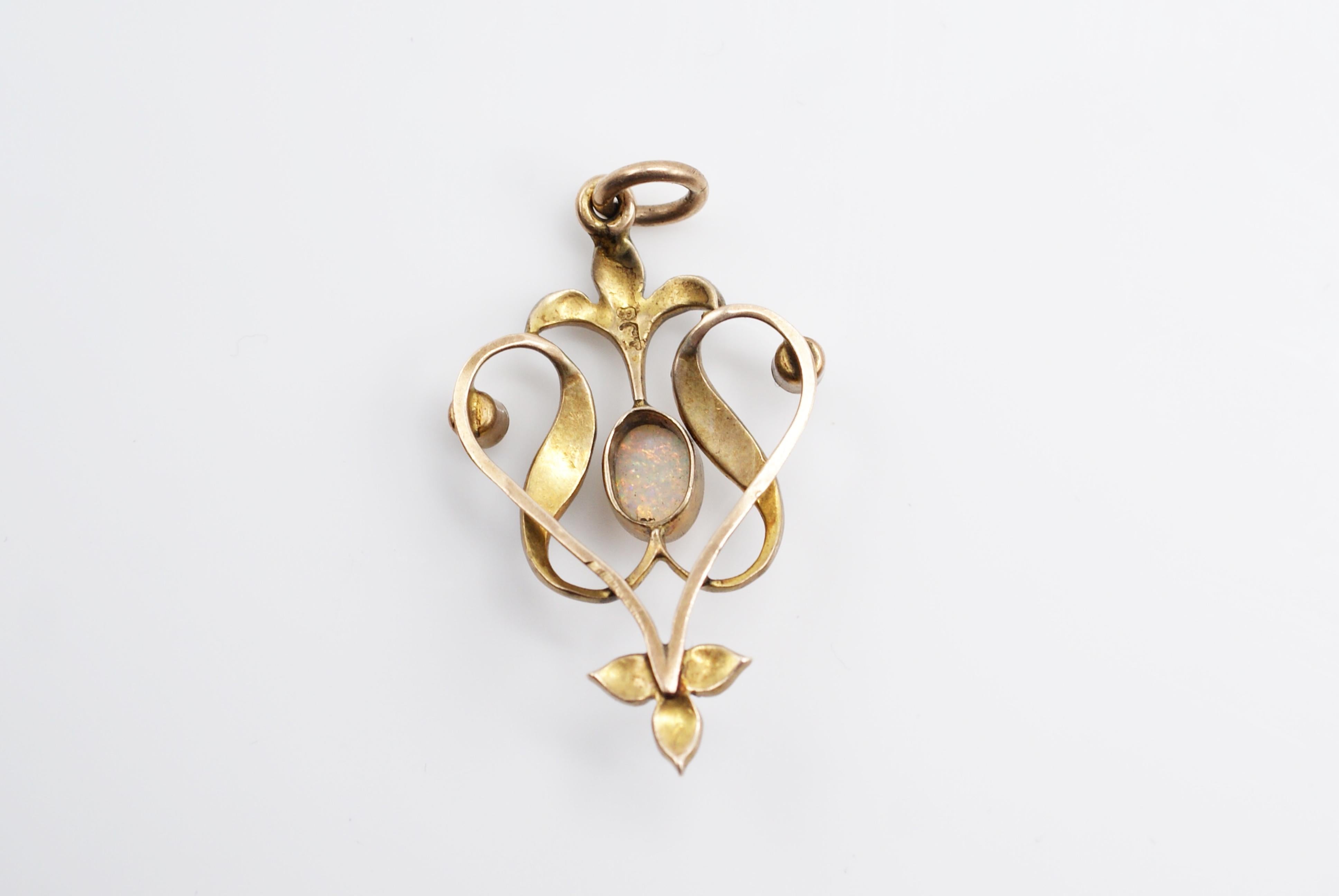 Beautifully handcrafted gold pendant from the turn of the century featuring one oval cabochon opal with amazing patches of red and orange. The flowing design of this pendant typical for this period is further embellished by small white lustrous seed