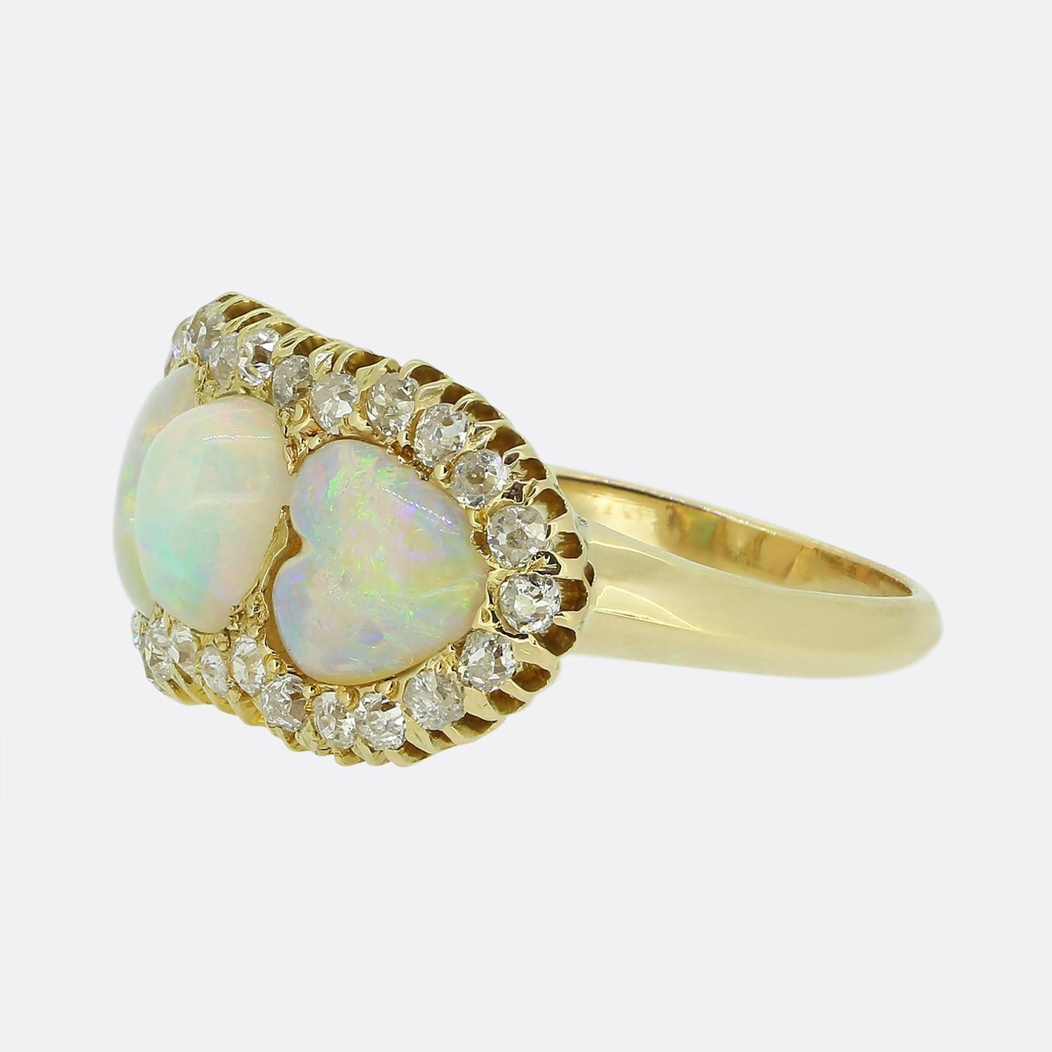 Here we have a striking Victorian ring crafted from 18ct yellow gold. The design showcases three white opals, one oval shaped and two heart-cuts, each with a captivating blue hue interspersed with flashes of greens and oranges. Surrounding the opals