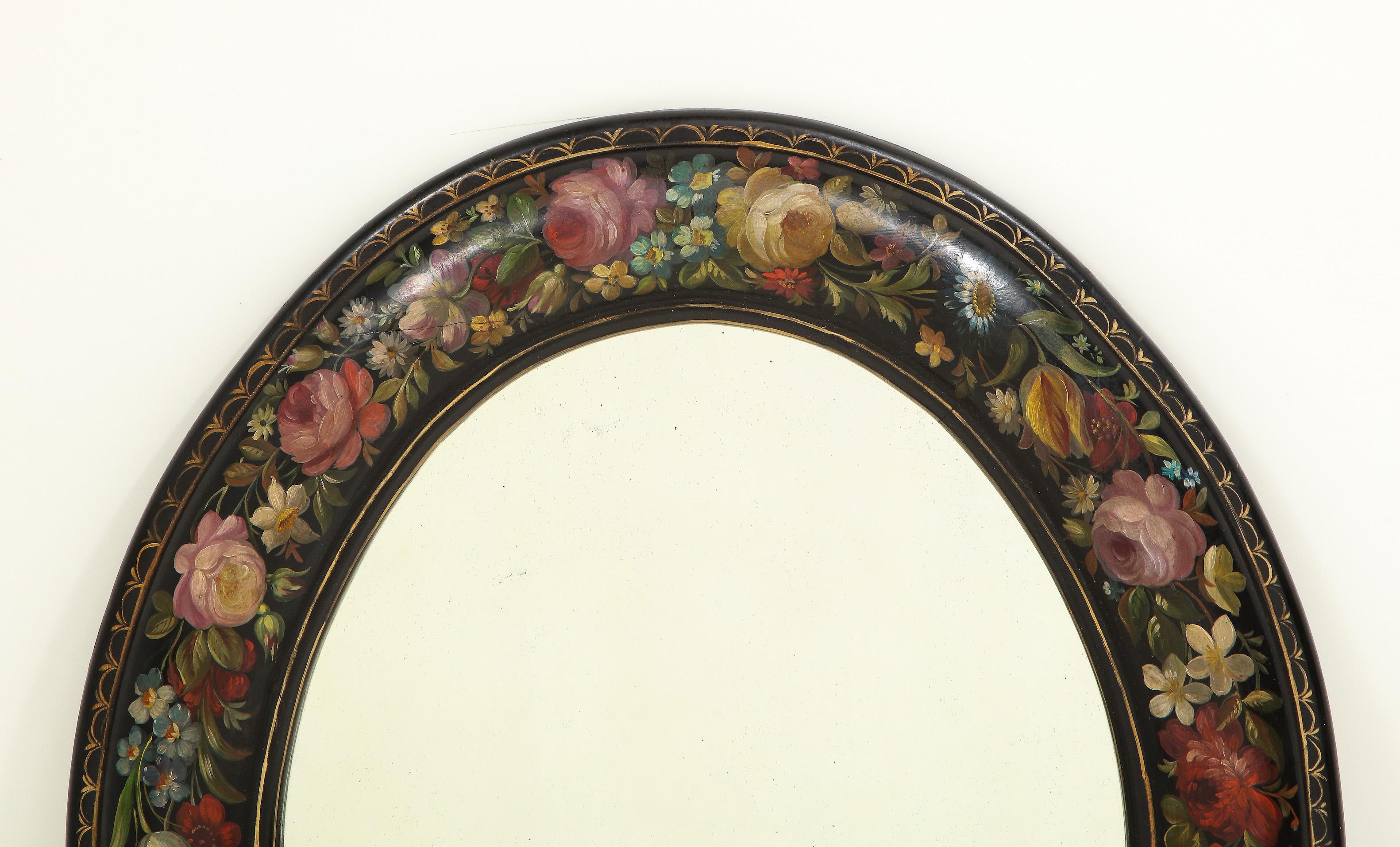The oval mirrored plate within a cushion frame lushly decorated with roses, daisies, daffodils and other floral sprays with a gilt egg and dart border, on a black ground.