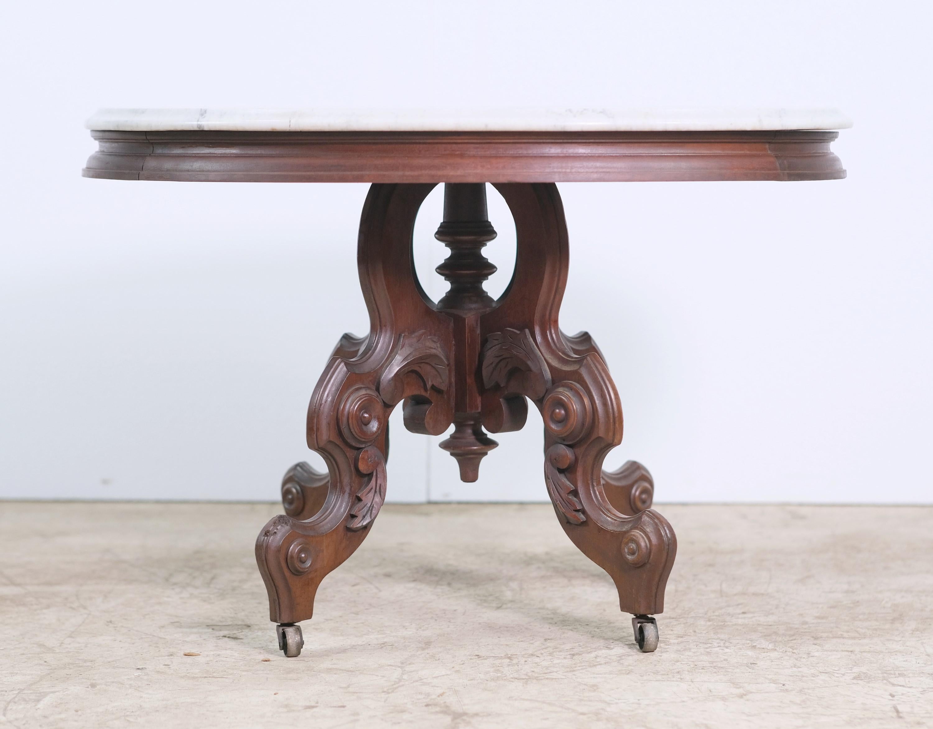 Early 20th century carved side table in an oval design. Features a white marble top with gray veining. Table base is done in a dark tone. Bulls eye details. Also this table features the original casters. This can be seen at our 400 Gilligan St