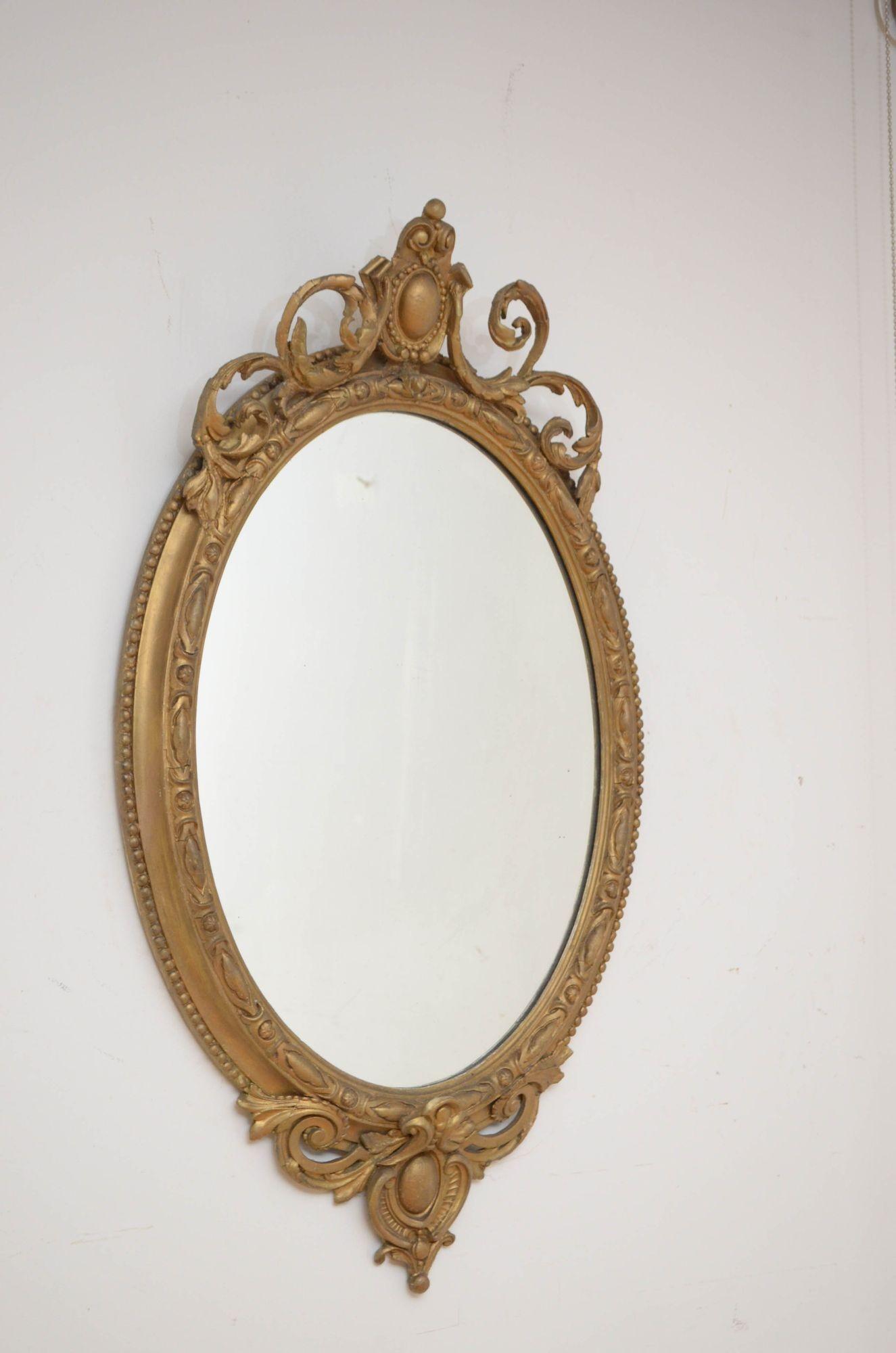 Sn5393 Victorian gilded wall mirror of oval form having original glass with minor imperfections in carved gilded frame with shaped crest to the base and top. This antique mirror has been refinished in gilt paste and is in home ready condition.