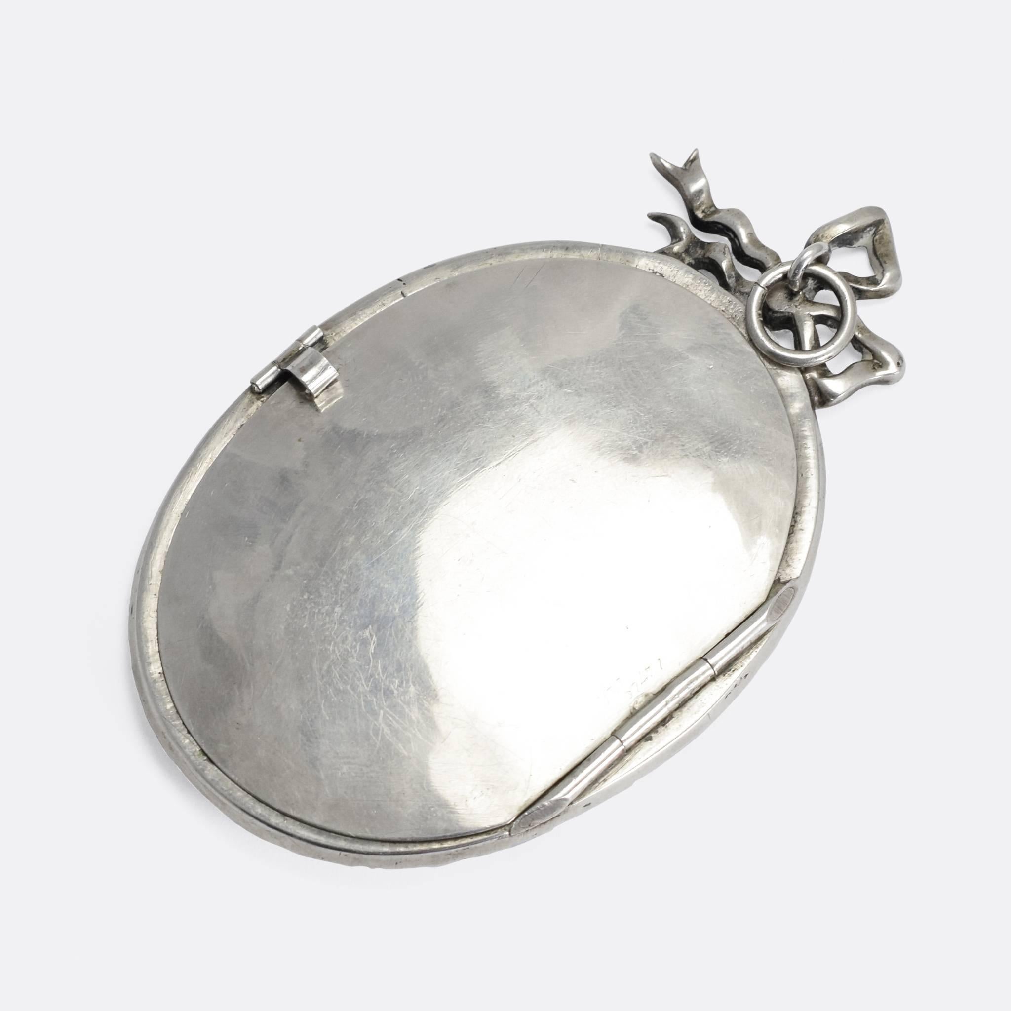 An oversized antique locket dating to c.1880. Modelled in Sterling silver throughout, this large scale piece features a border of white paste gemstones, and an offset bow at the top. The back opens up, allowing for the display of a photograph or