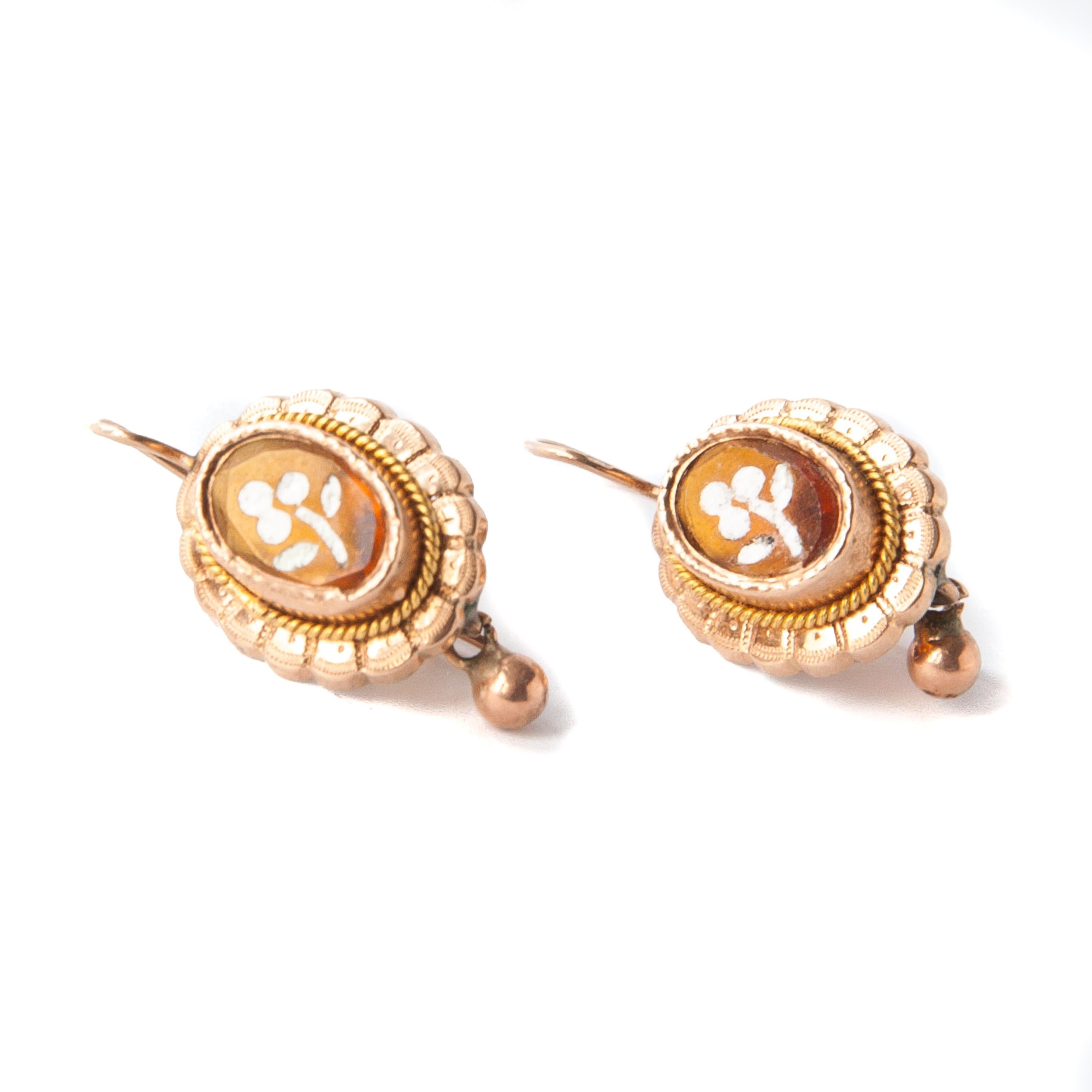 Elegant pair of 14 karat gold Victorian drop earrings. The earrings are inlaid with honey colored citrine. The citrine gemstone has a small white painted flower at the front of the earrings. They are oval-shaped and have a little bell dangling below