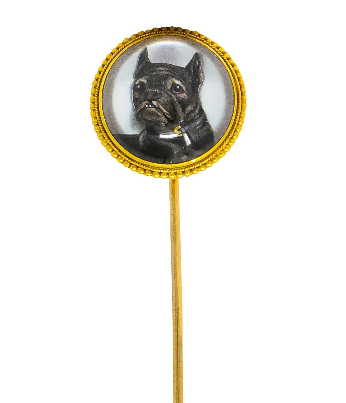 Centering a round rock crystal cabochon measuring approximately 16.8 mm, bezel set, in a millegrain and beaded gold surround

With a reverse carved intaglio depiction of a French Bulldog, hand-painted with a dark grey fur-coat, chestnut brown eyes,