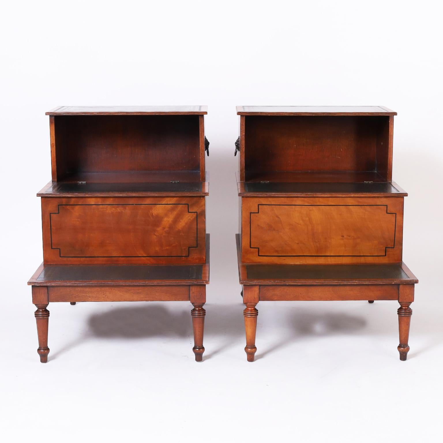 Handsome pair of antique English library step form stands crafted in mahogany with tooled green leather steps, storage under the middle, brass lion head hardware, and classic turned legs.