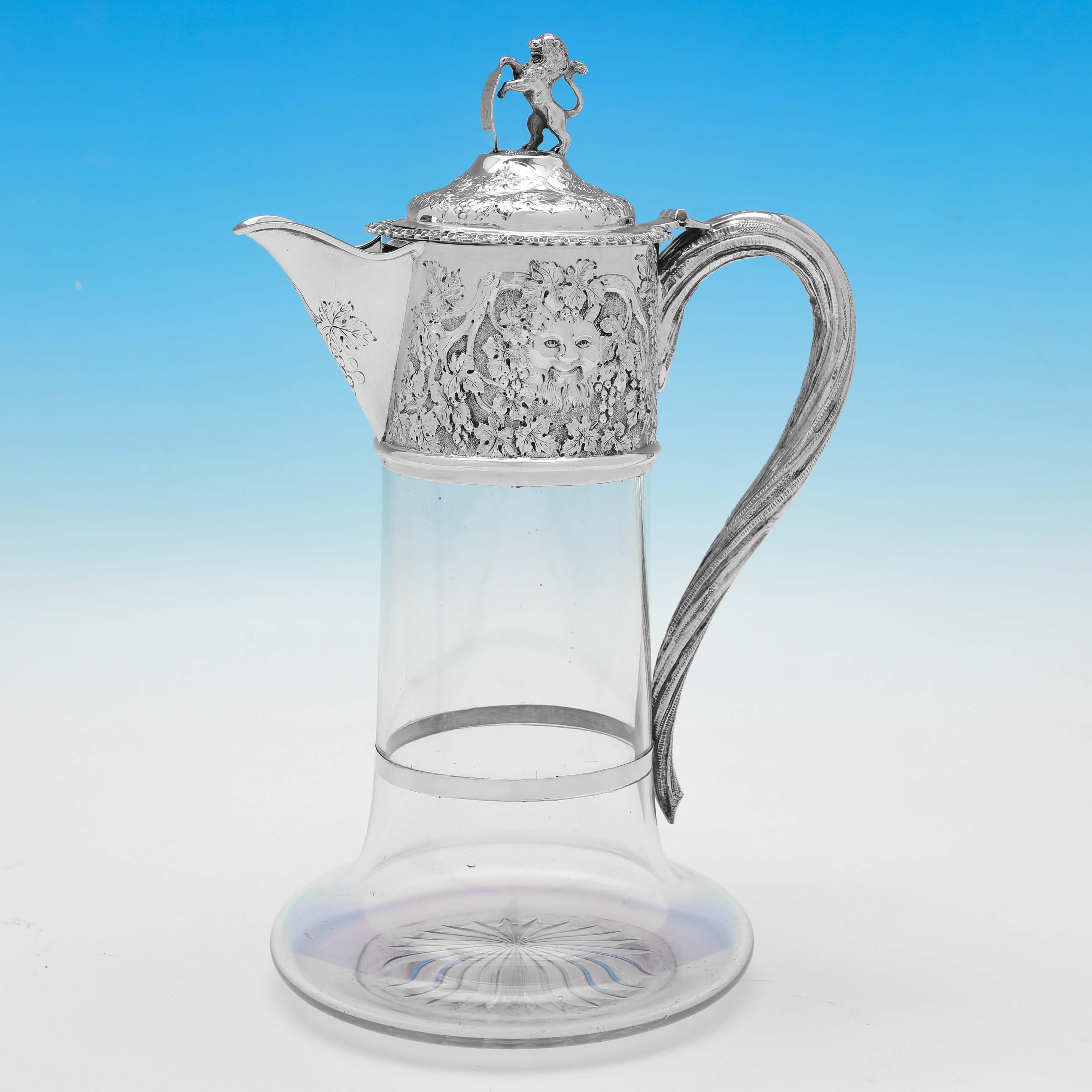 Hallmarked in London in 1874 by Charles Boyton, this striking and rare, Victorian, Antique Sterling Silver Pair of Claret Jugs, feature plain glass bodies, and ornate silver mounts with bacchus masks and grape and vine decoration, and finials of