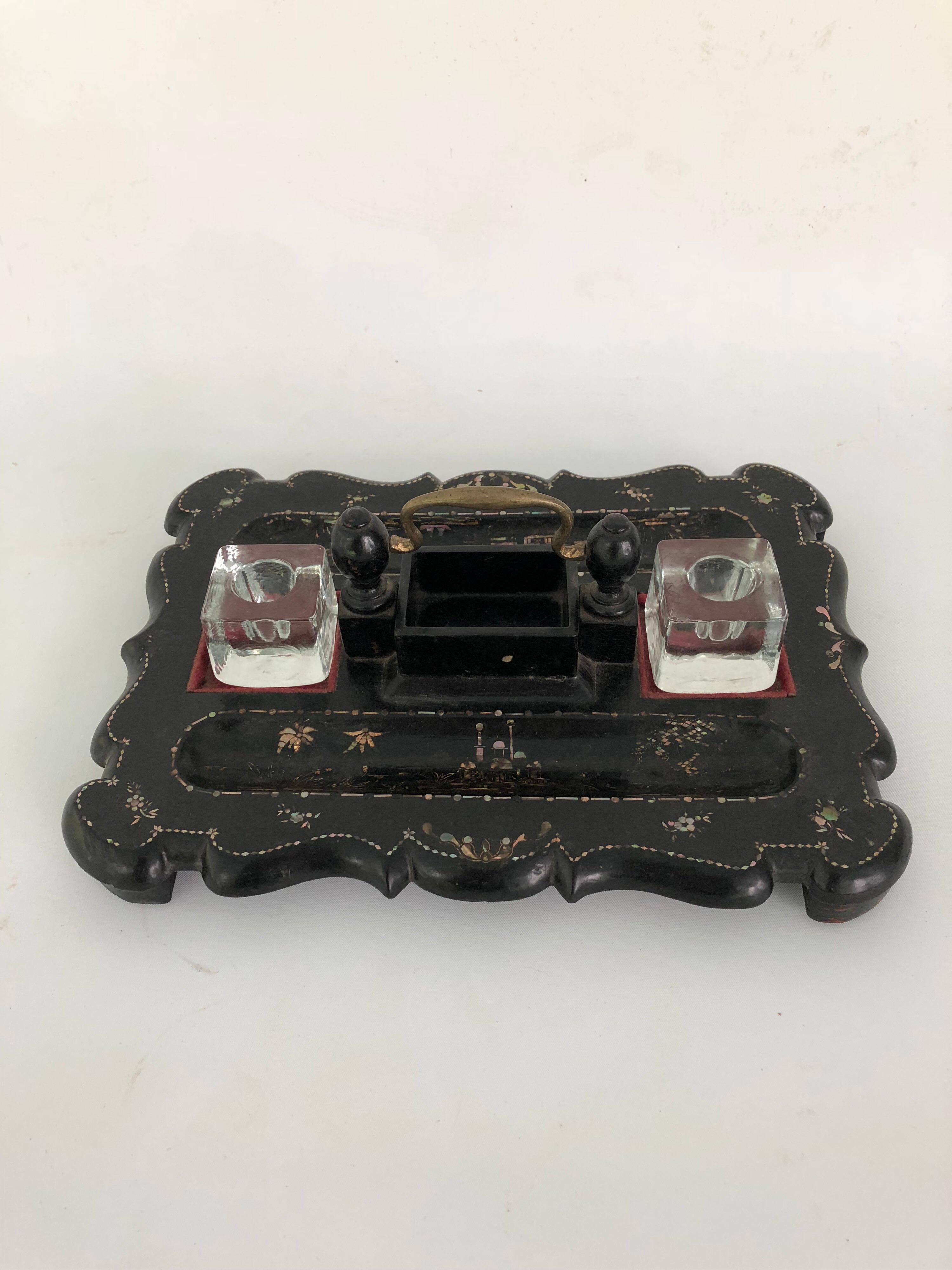 Victorian black lacquer papier mache pen and ink stand with gold and mother-of-pearl inlay decoration.
Two inkwell Stand areas covered in red felt. Brass handle and two glass ink pots. Marked in gold pen on the underside 4 Leadenhall Street,