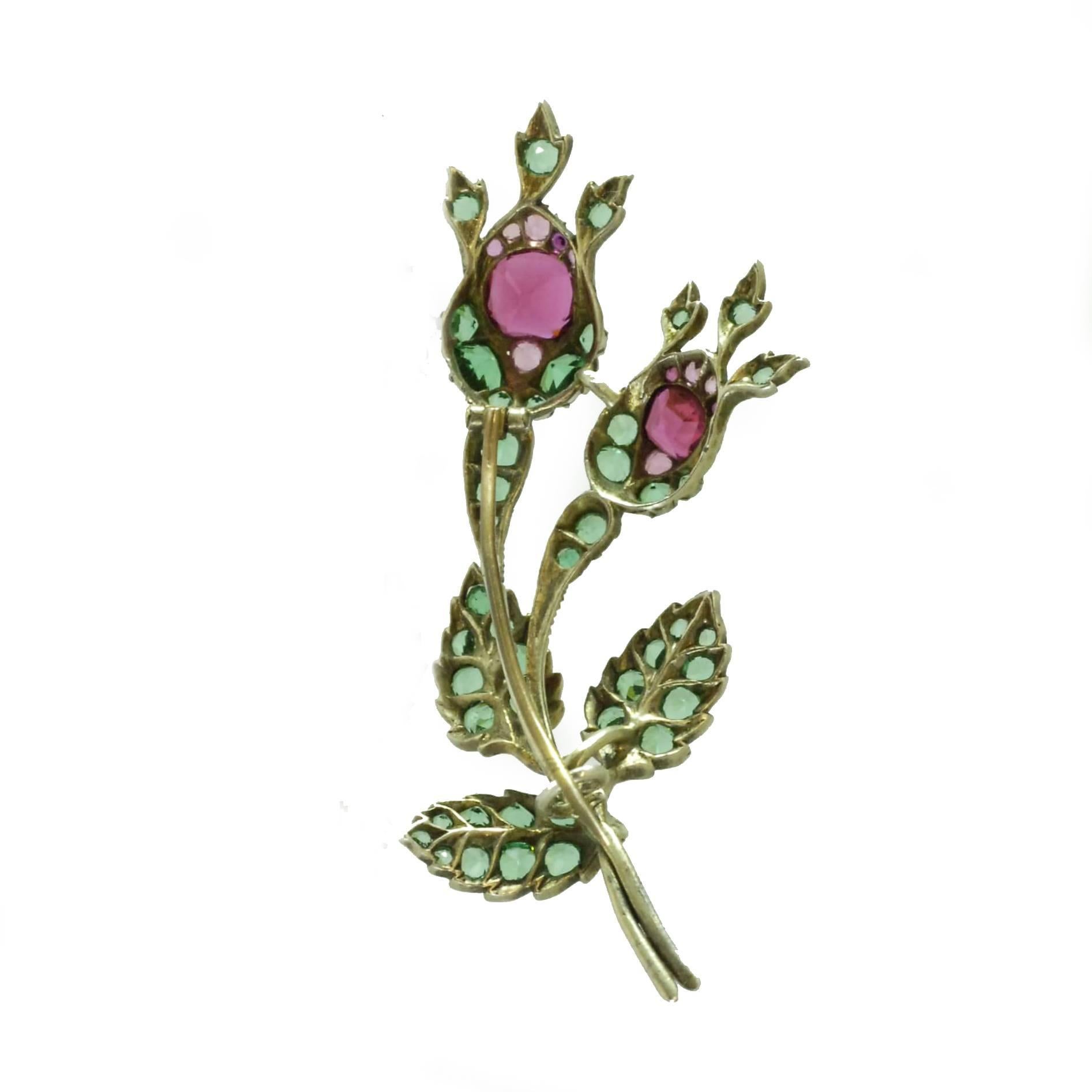 A brooch in the form of a rose bud sprig set with green and red paste. Mounted in silver and gilt metal. English, circa 1850.