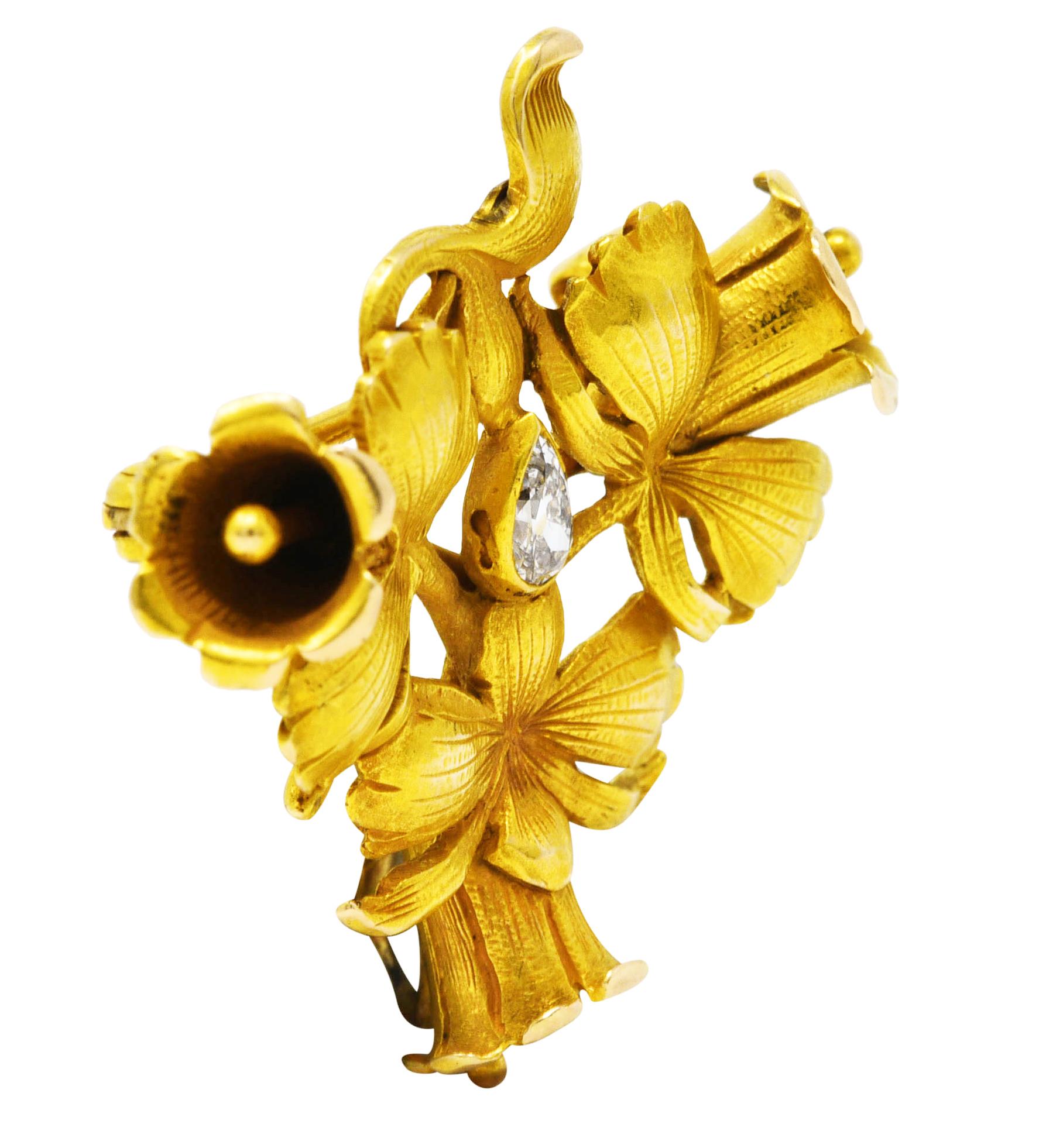 Brooch is designed as three stylized trumpet flowers. Highly rendered, dimensional, and texturous. Centering a bezel set pear cut diamond. Weighing approximately 0.15 carat with G color and VS clarity. Completed by a pin stem with locking closure