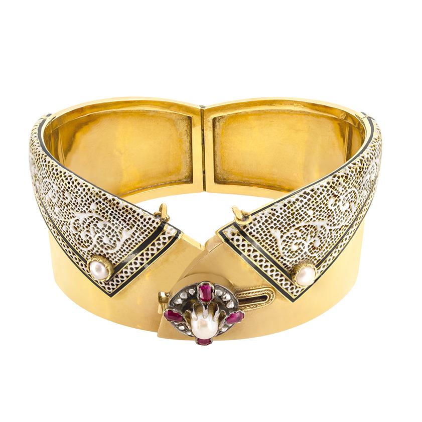 This uniquely designed bangle dates to the Victorian period. Crafted in 18 carat yellow gold the the piece features a central 5.3mm pearl surrounded by a halo four rubies, each weighing 0.10 carat, and twelve rose cut diamonds totalling 0.12 carat.