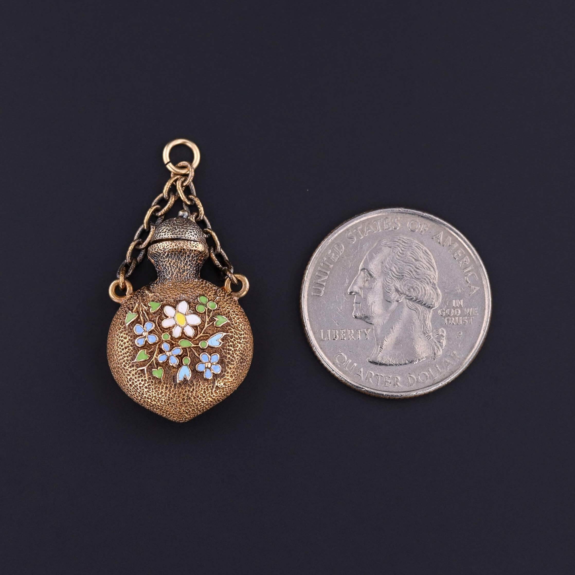 Questo ciondolo, uno squisito tesoro dell'epoca vittoriana (circa 1880), assume la forma di una bottiglia di profumo in miniatura realizzata in oro massiccio 14k. È splendidamente ornata da fiori smaltati dipinti a mano su entrambi i lati, con ogni