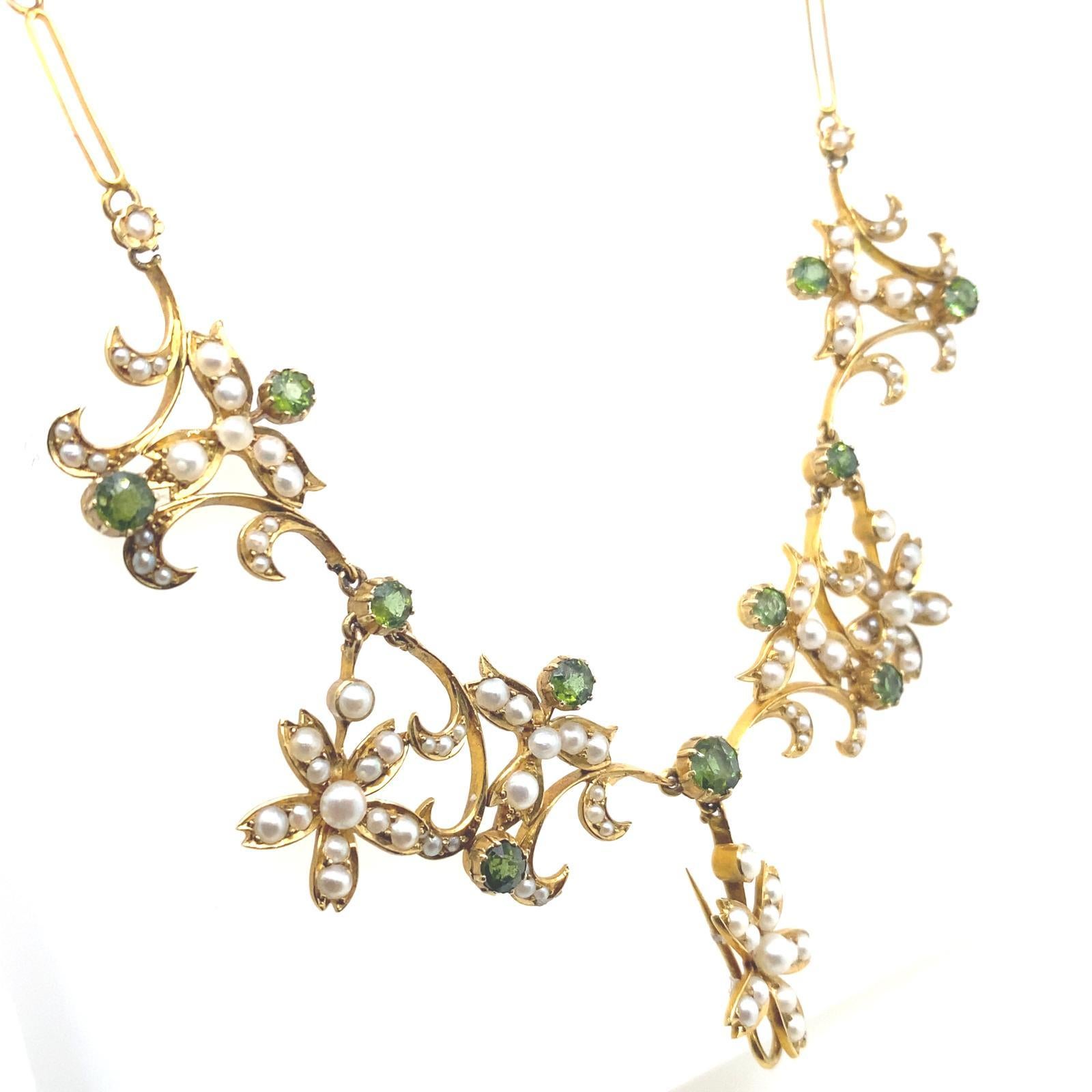 A Victorian peridot and seed pearl necklace in 18 karat yellow gold.

This pretty necklace is designed as a series of  flowers and scrolled motifs set with seed pearls and illusion set round cut peridot gemstones.

The necklace is crafted in 18