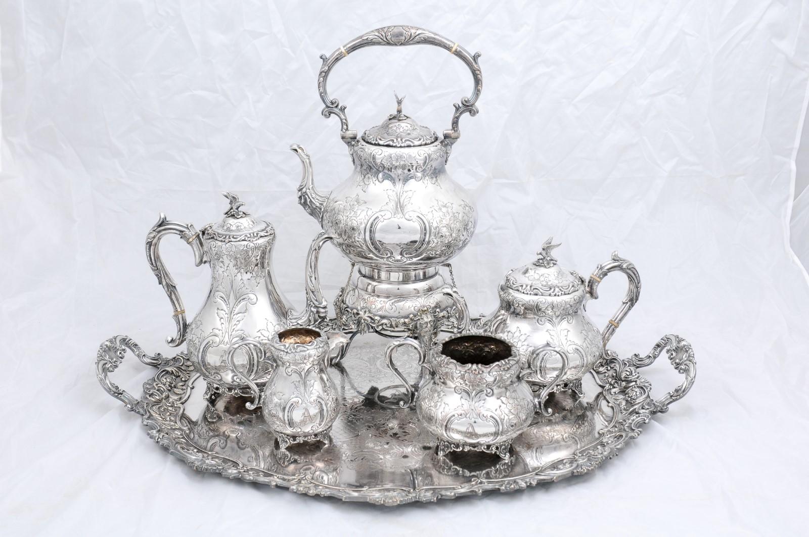 A Victorian period five-piece English silver tea and coffee set from the 19th century with tray. Created in England during the reign of Queen Victoria, this silver tea and coffee set features a spirit kettle (teapot resting on a burner), a coffee