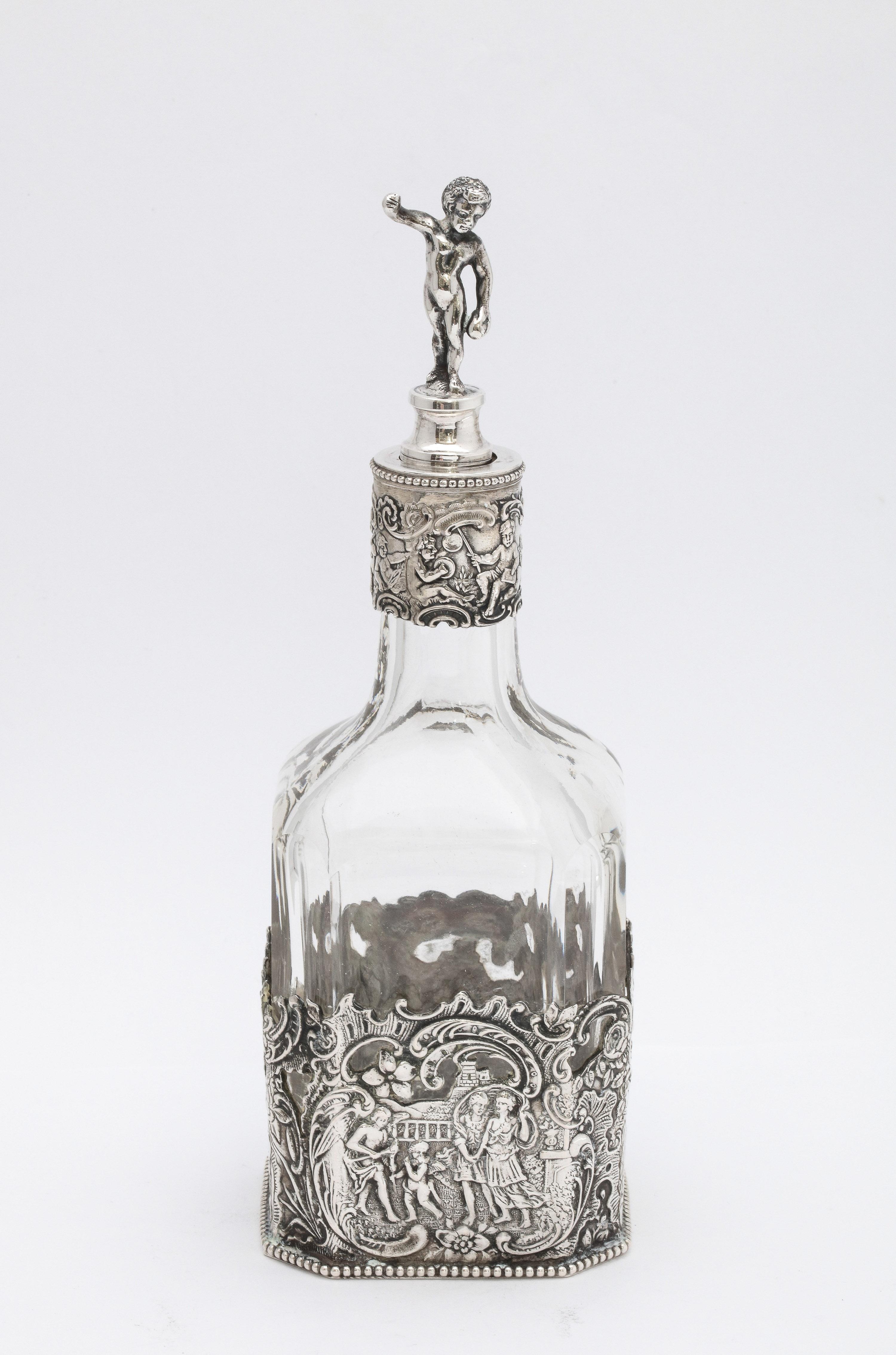 Victorian period, Continental Silver (.800) - mounted glass liqueur decanter, Germany -- Hanau. Silver is depicts country scenes with couples dancing, etc. Measures 8 1/4 inches high to top of figure on top 
of stopper x 3 inches wide (at widest