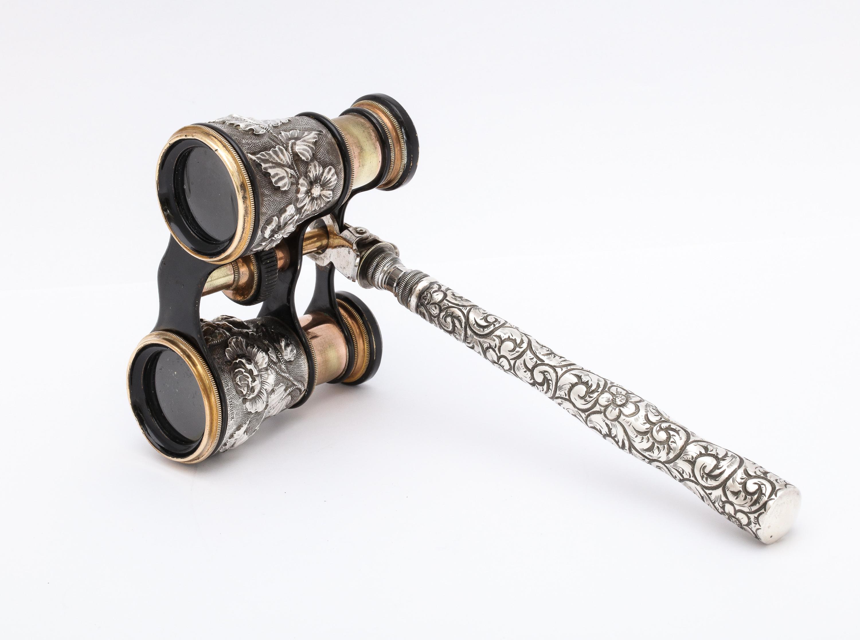 Rare pair of sterling silver opera glasses/binoculars, England, Ca. 1890's. The handle, which is removable, measures 7 inches from tip to tip. Adjustable opera glasses measure 4 inches wide x 3 1/4 inches deep when lenses are fully extended x 2 1/4