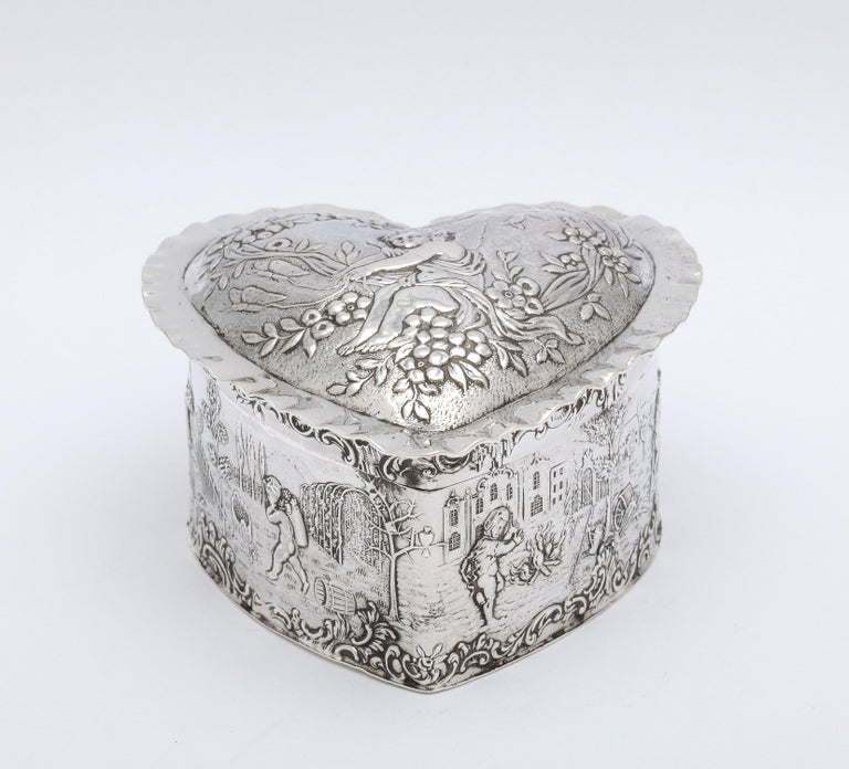 Lovely, Victorian Period, sterling silver heart-form trinkets box with hinged lid and gilt interior, London, year-hallmarked for 1898, John George Smith - maker. Bears foreign import Hanau marks on its underside. Lid is decorated with a cherub