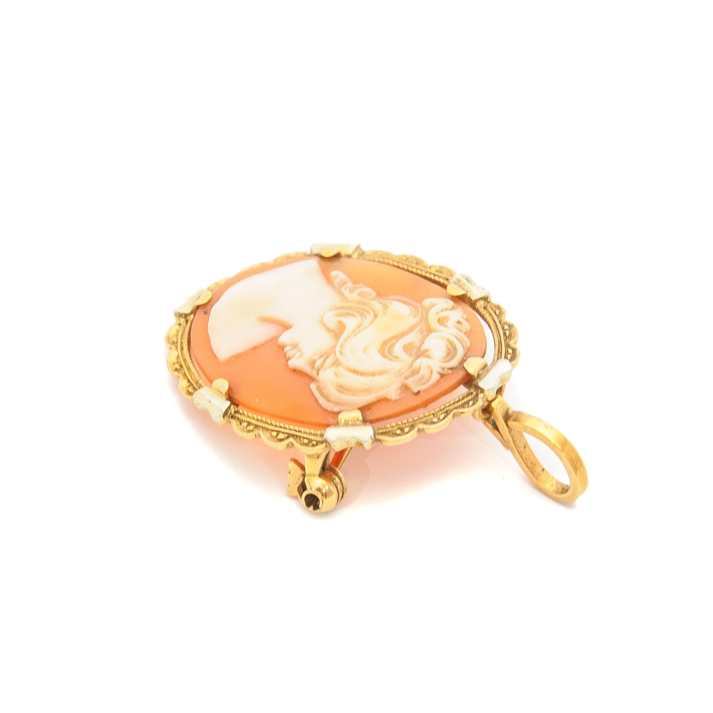 A mid-century vintage cameo brooch pendant made of shell and gold. The shell cameo is beautifully carved into this female silhouette. The color of the cameo is pinkish, slightly orangish and set in a 18 karat yellow frame. The 18 karat gold mounting