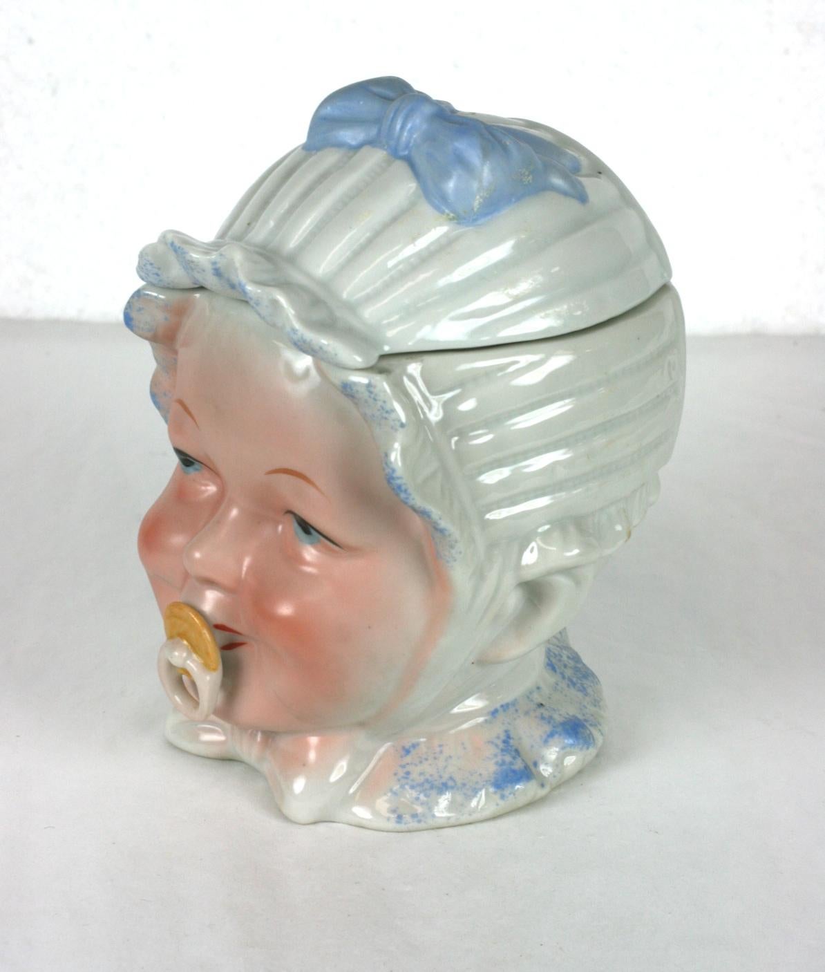 Victorian porcelain baby's head dresser jar or humidor likely made by Heubach, Germany circa 1880 to 1900. The antique porcelain dresser jar is in the shape of happy baby's head with a mouth pacifier and a blue and white bonnet with a blue ribbon.