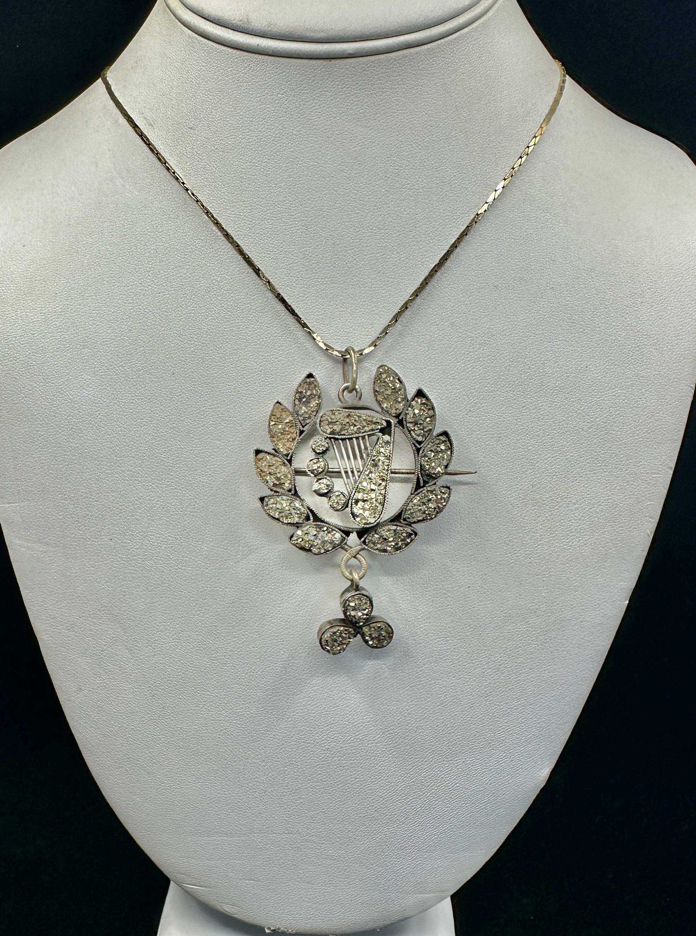 Lasciati conquistare da questa rara e romantica collana o spilla con ciondolo in pirite druzy dell'epoca vittoriana, che ha la forma di un'arpa a lira circondata da una corona d'alloro con un pendente a forma di trifoglio.  La spilla è un omaggio al