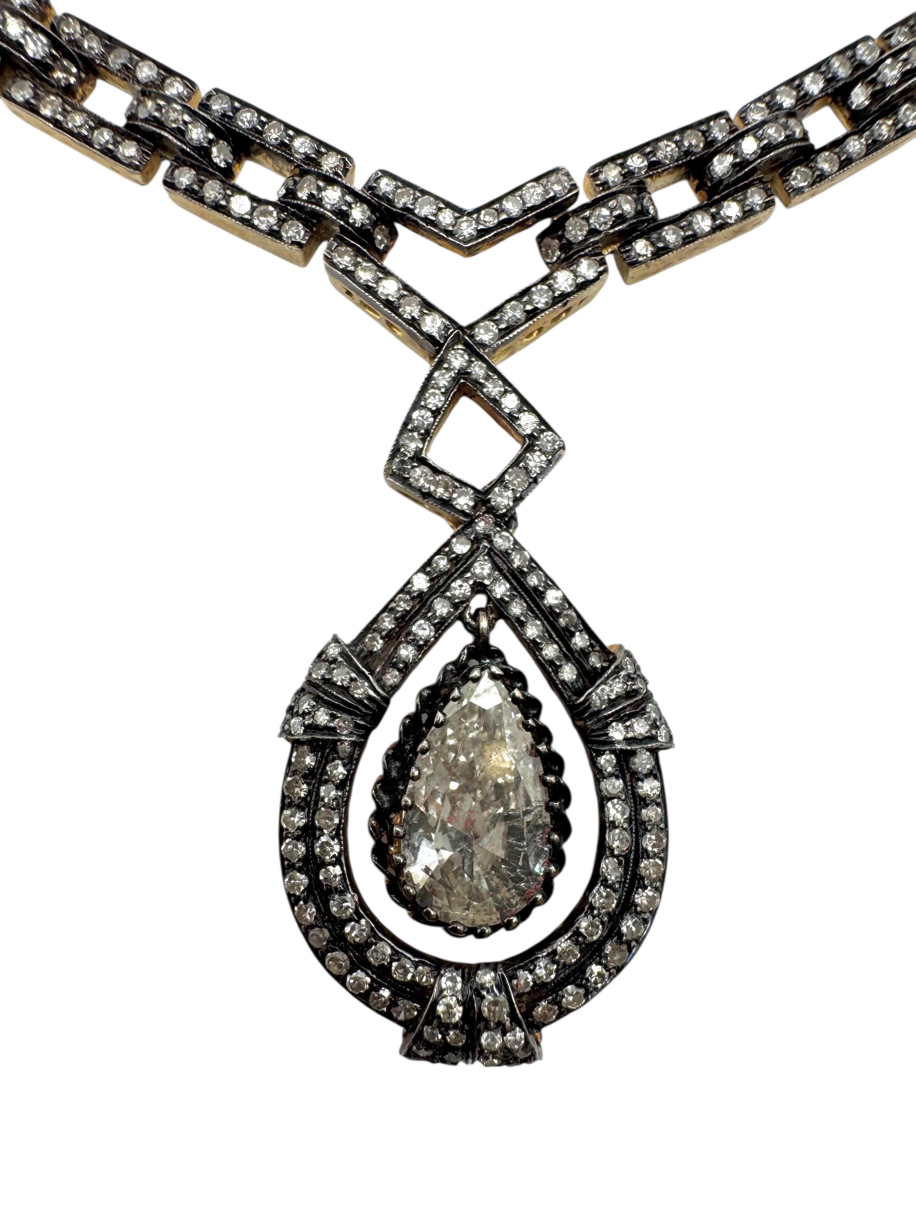 Una collana audace e regale in oro giallo 18 carati e argento, disegnata in stile revival vittoriano. Il centro è caratterizzato da un sorprendente diamante a forma di pera da 2,54 carati incorniciato da doppie aureole di diamanti, sospeso da una