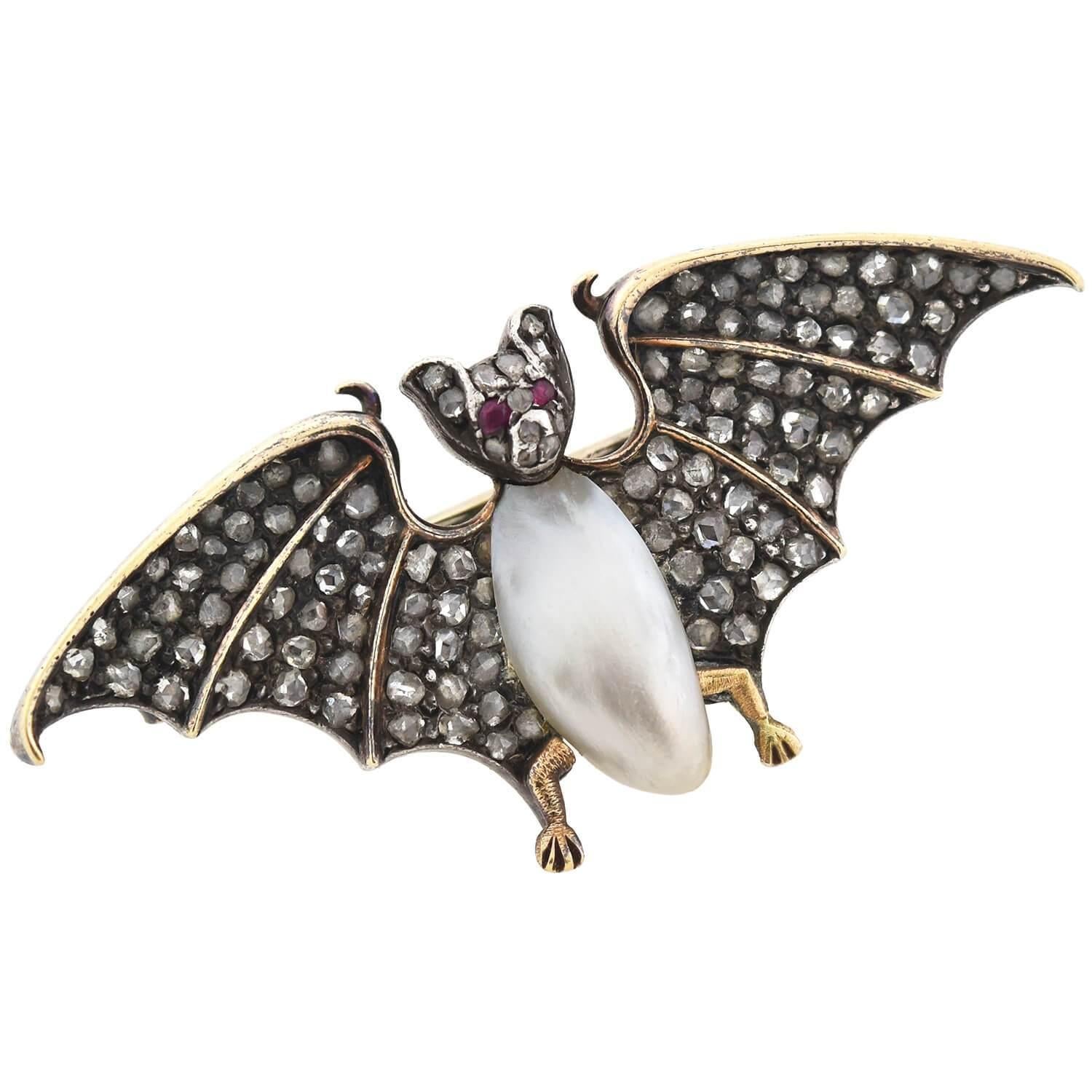 An rare and exquisite gemstone bat pin from the Victorian (ca1880) era! Crafted in 18kt yellow gold topped with sterling silver, this mixed metals piece depicts an open winged bat, which comes to life in realistic 3-dimensional detail. Its