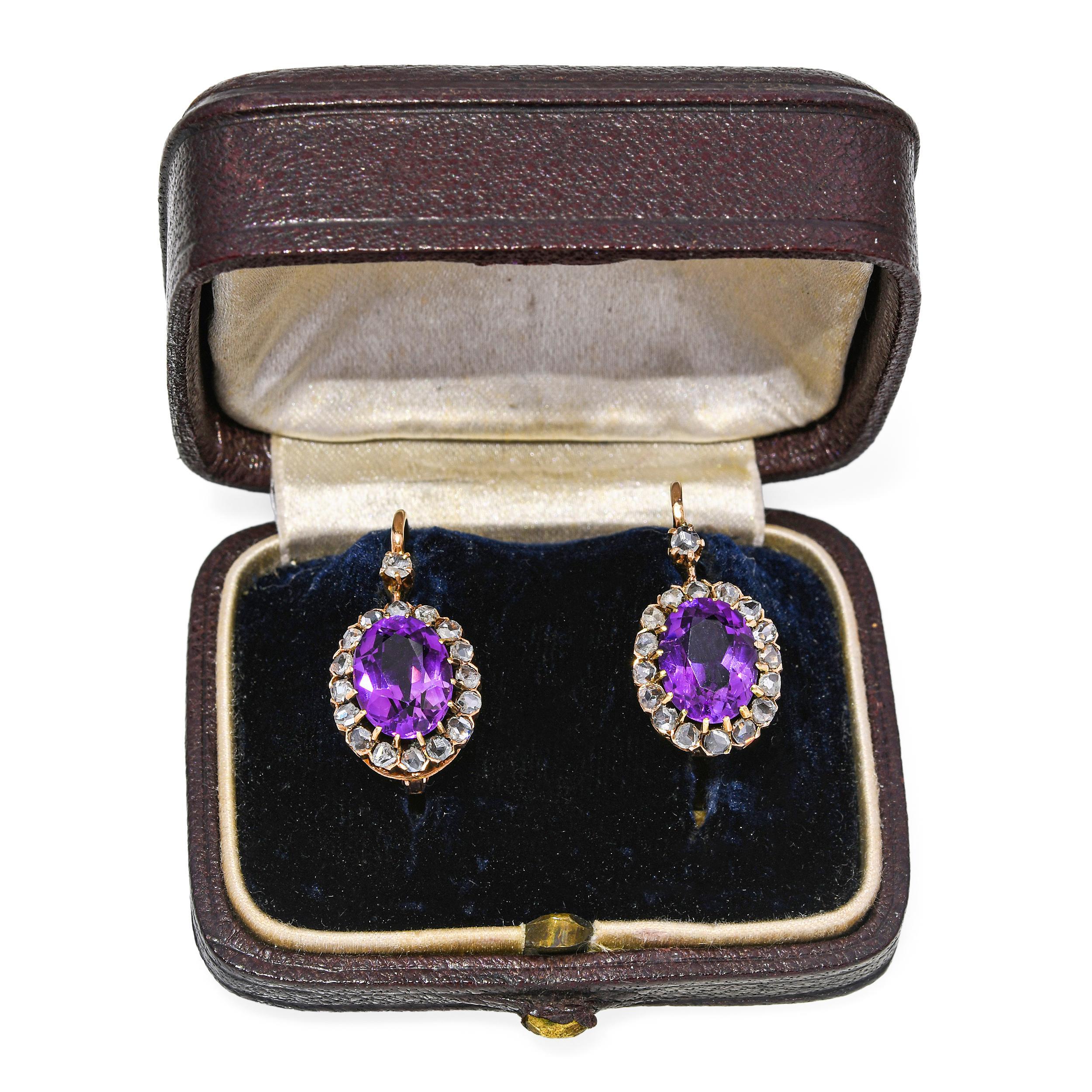 Une paire de boucles d'oreilles victoriennes saisissantes, chacune centrée sur une améthyste de taille ovale richement colorée et d'une vibrance exceptionnelle. Les pierres violettes sont encadrées par des halos de diamants taillés en rose, dont